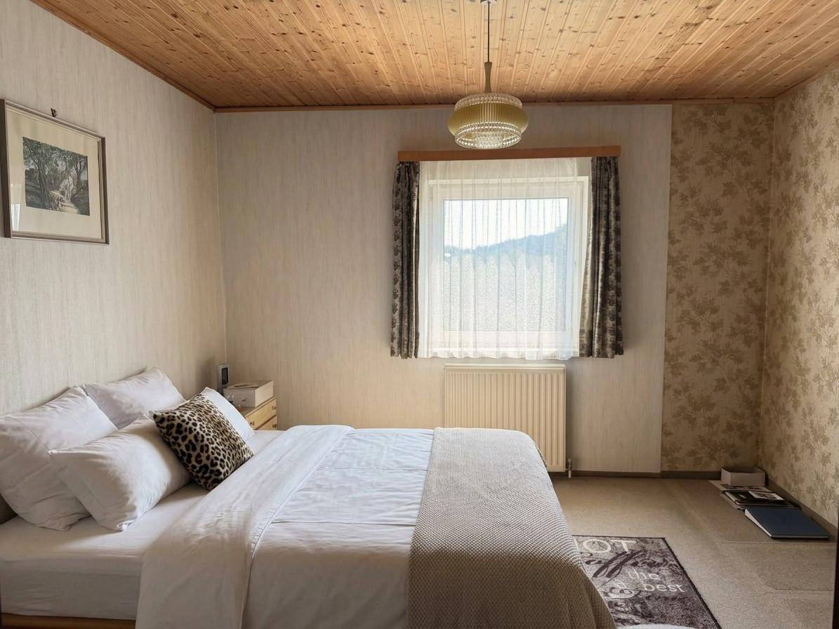 Schlafzimmer mit Doppelbett, gemusterter Tapete, Holzdecke und einem Fenster mit Blick auf die Landschaft.