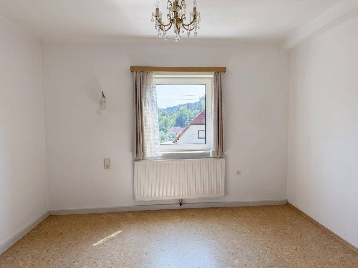 Heller, leerer Raum mit weißen Wänden, einem Fenster und einem Kronleuchter, bereit zur individuellen Gestaltung.