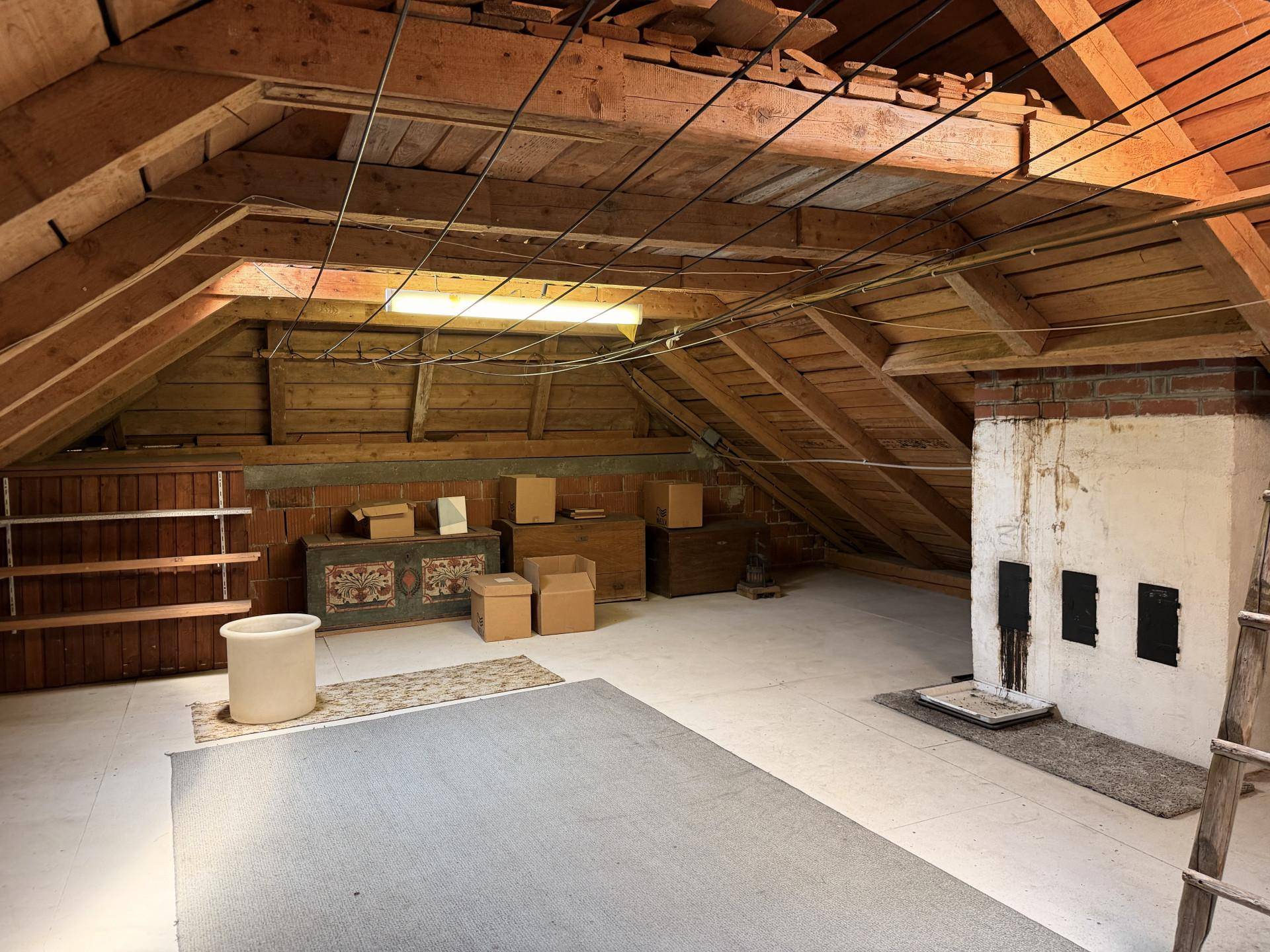 Geräumiger Dachboden mit sichtbaren Holzbalken und einem traditionellen Kachelofen, ideal als Lagerraum.