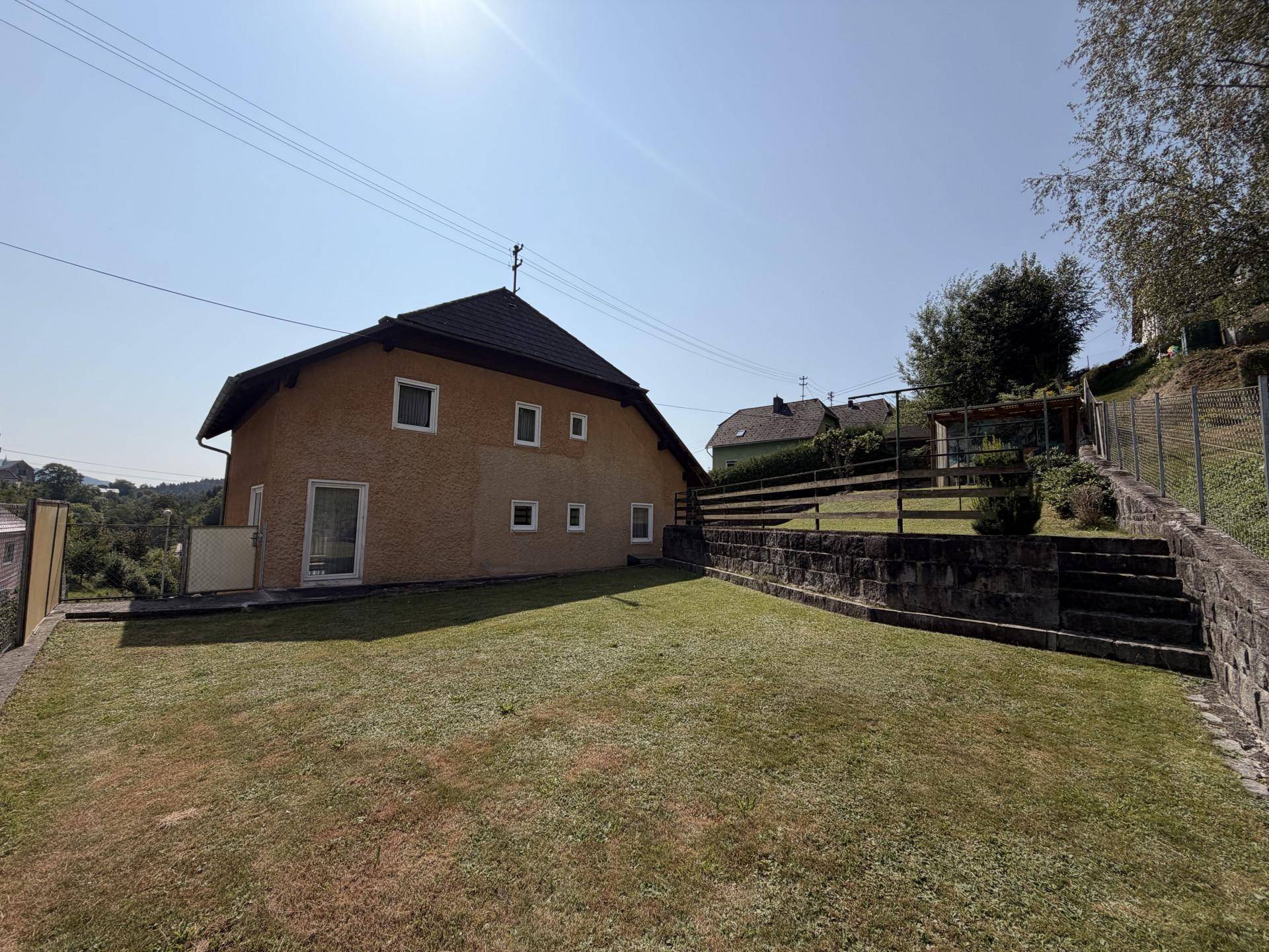 Seitenansicht des Hauses mit gepflegtem Rasen und einer stabilen Steinmauer im Gartenbereich.