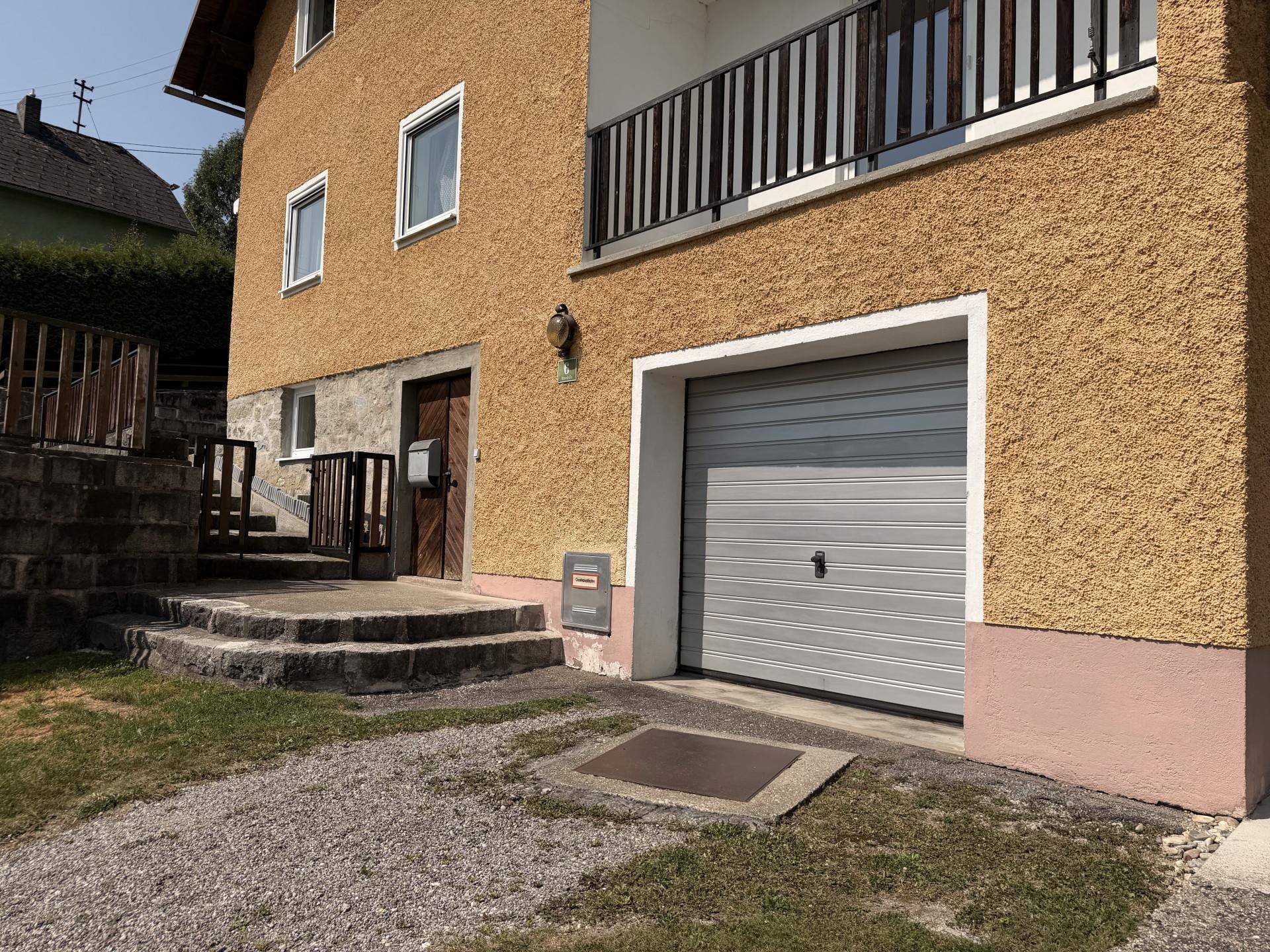 Hauseingang mit grauer Garagentür, Steinstufen und gelber Fassade, einladend gestaltet.