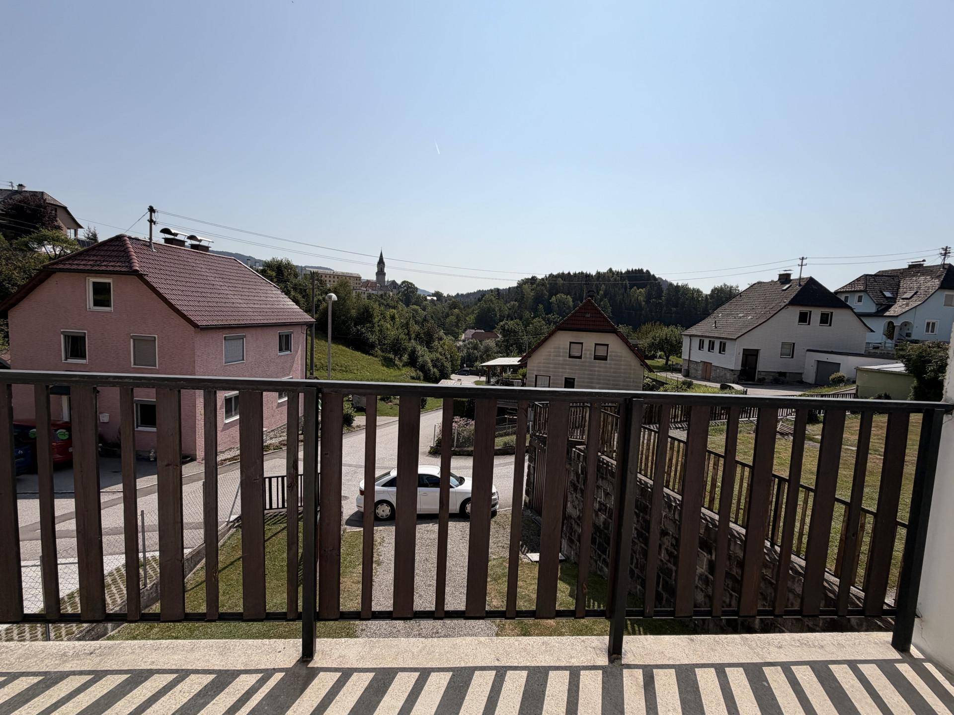 Ausblick vom Balkon auf die umliegende Wohngegend mit Häusern, Straße und einem Kirchturm in der Ferne.