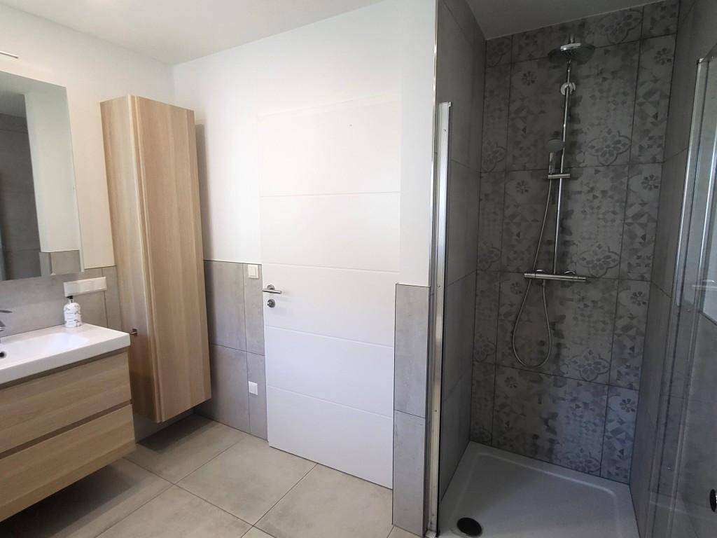 Helles Badezimmer mit Duschkabine, modernem Waschtisch und praktischem Hochschrank.
