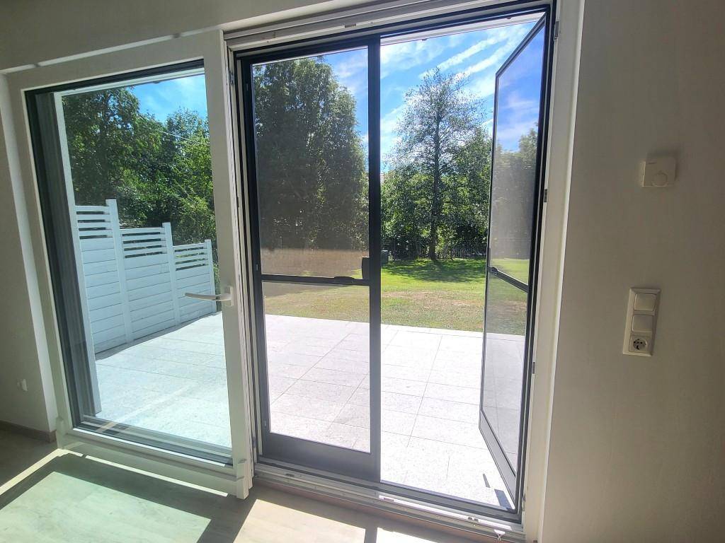 Große Glasschiebetür bietet Zugang zu einer gepflasterten Terrasse und dem weitläufigen Garten.