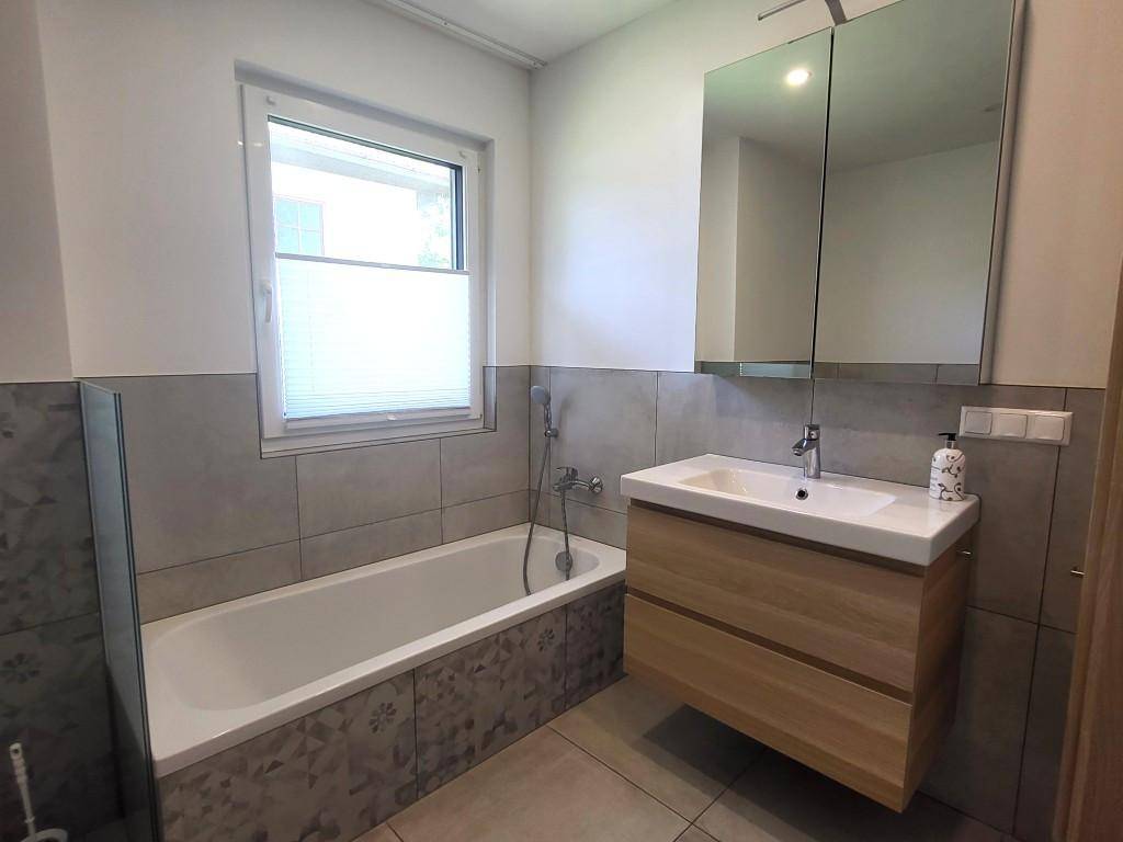 Modernes Badezimmer mit Badewanne, schwebendem Waschtisch, Spiegelschrank und Fenster.
