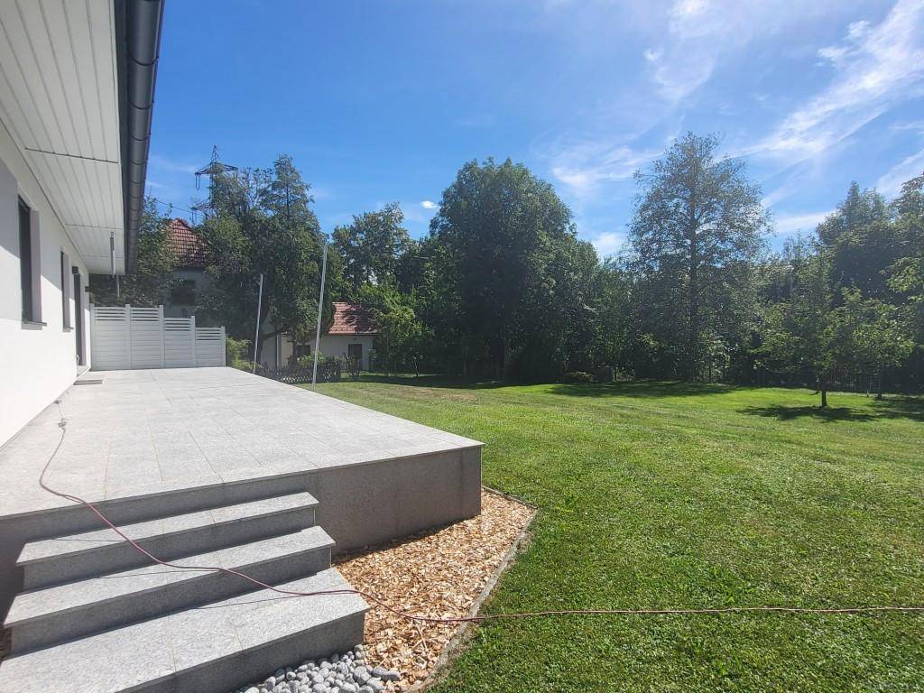 Große, sonnige Terrasse mit Steinstufen, die zu einem weitläufigen grünen Garten führen.