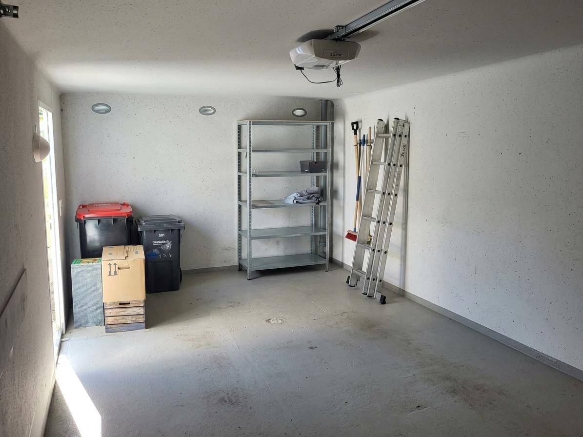 Geräumige Garage mit Betonboden, Regalen und Platz für Werkzeuge und Fahrzeuge.