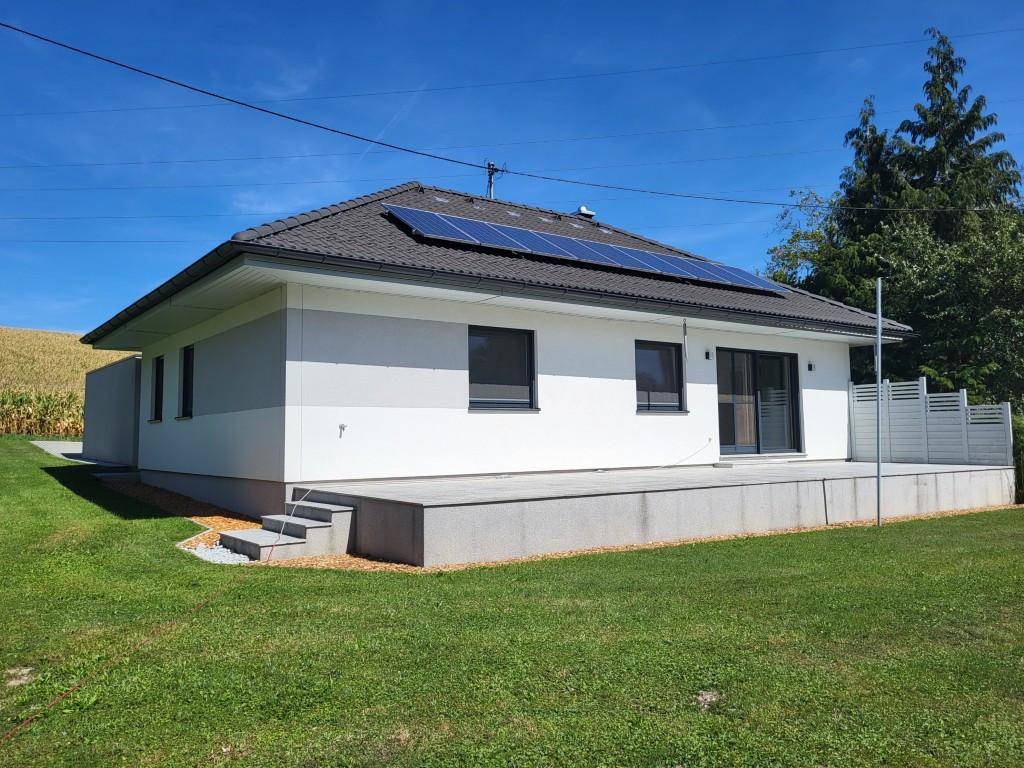 Rückansicht des Hauses mit großer Terrasse, weitläufigem Garten und Photovoltaikanlage auf dem Dach.