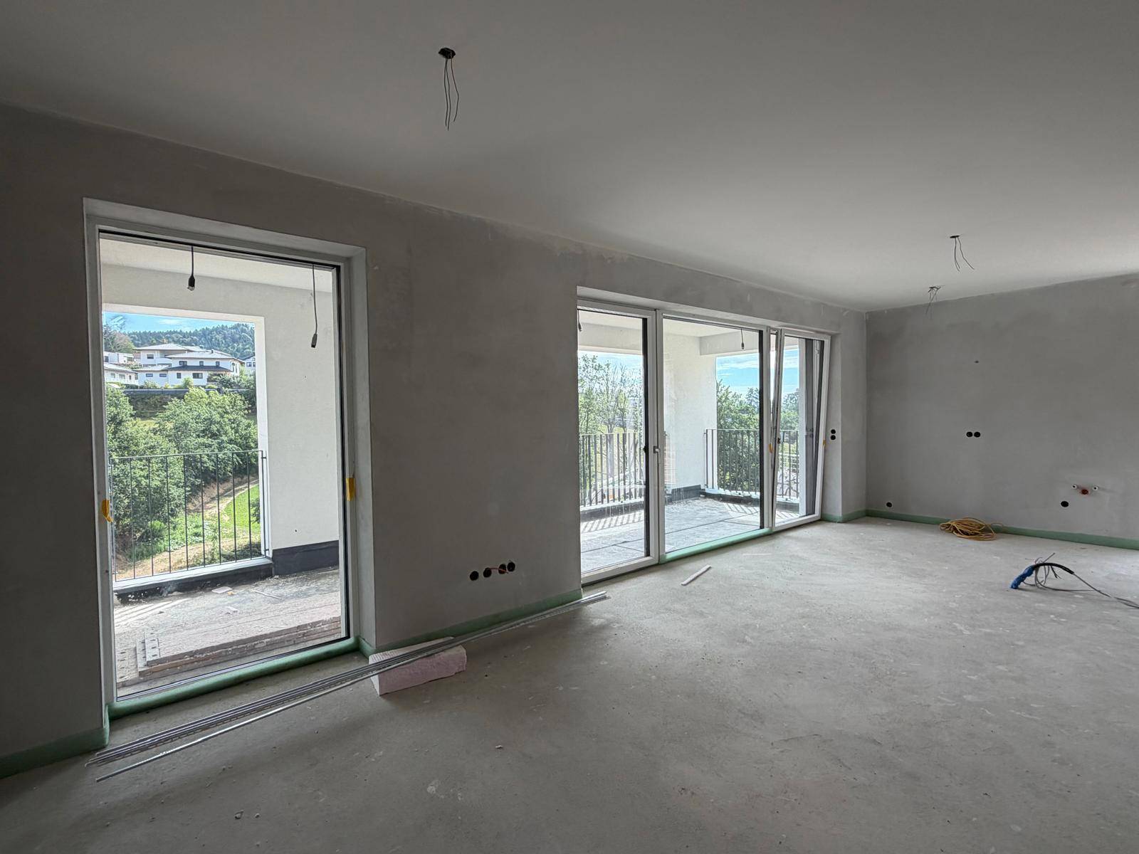 Heller, unfertiger Wohnraum mit großen Fenstern und Zugang zu einem Balkon.