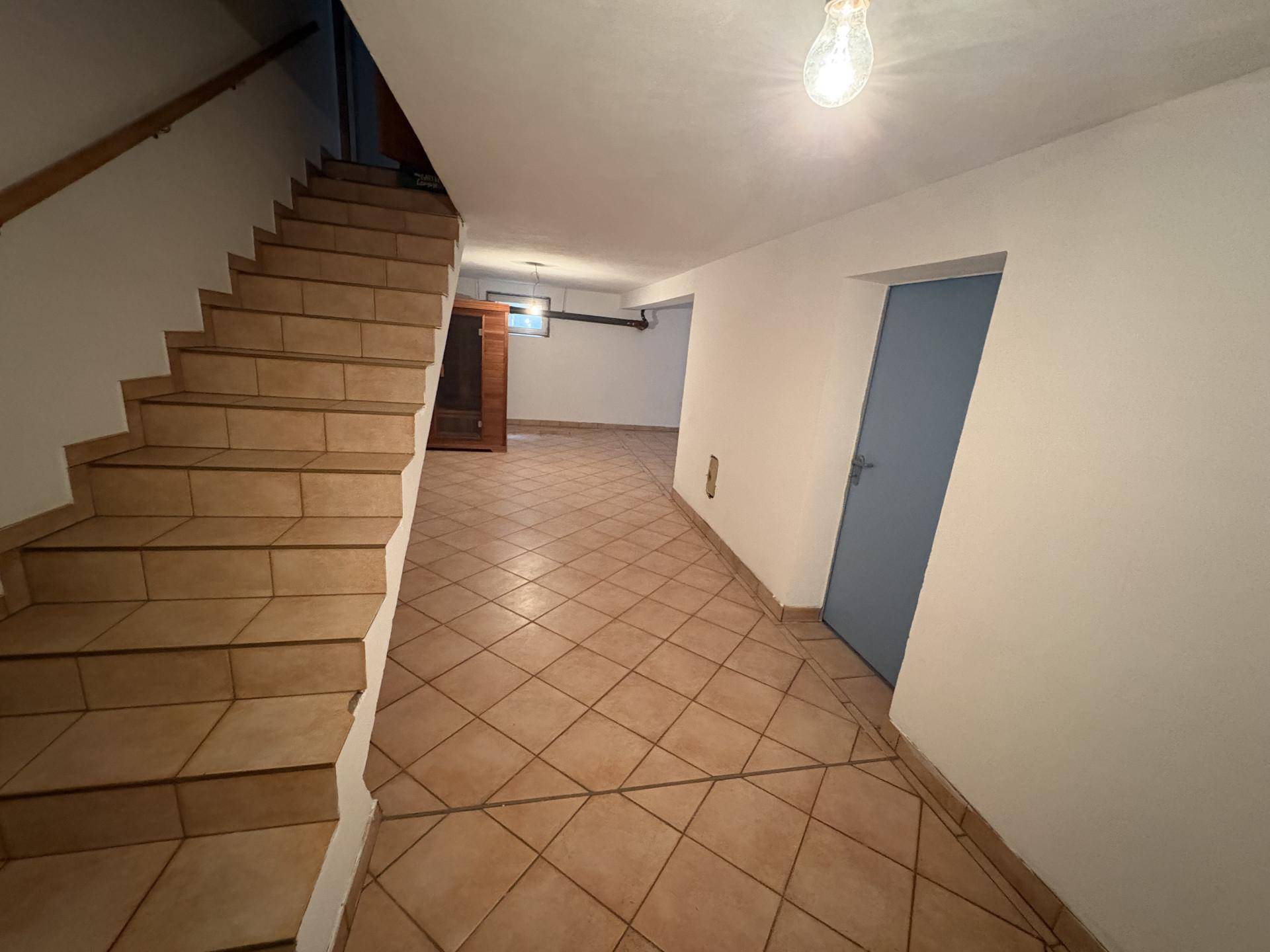Kellerflur mit gefliestem Boden und Treppe, bietet Zugang zu weiteren Kellerräumen.
