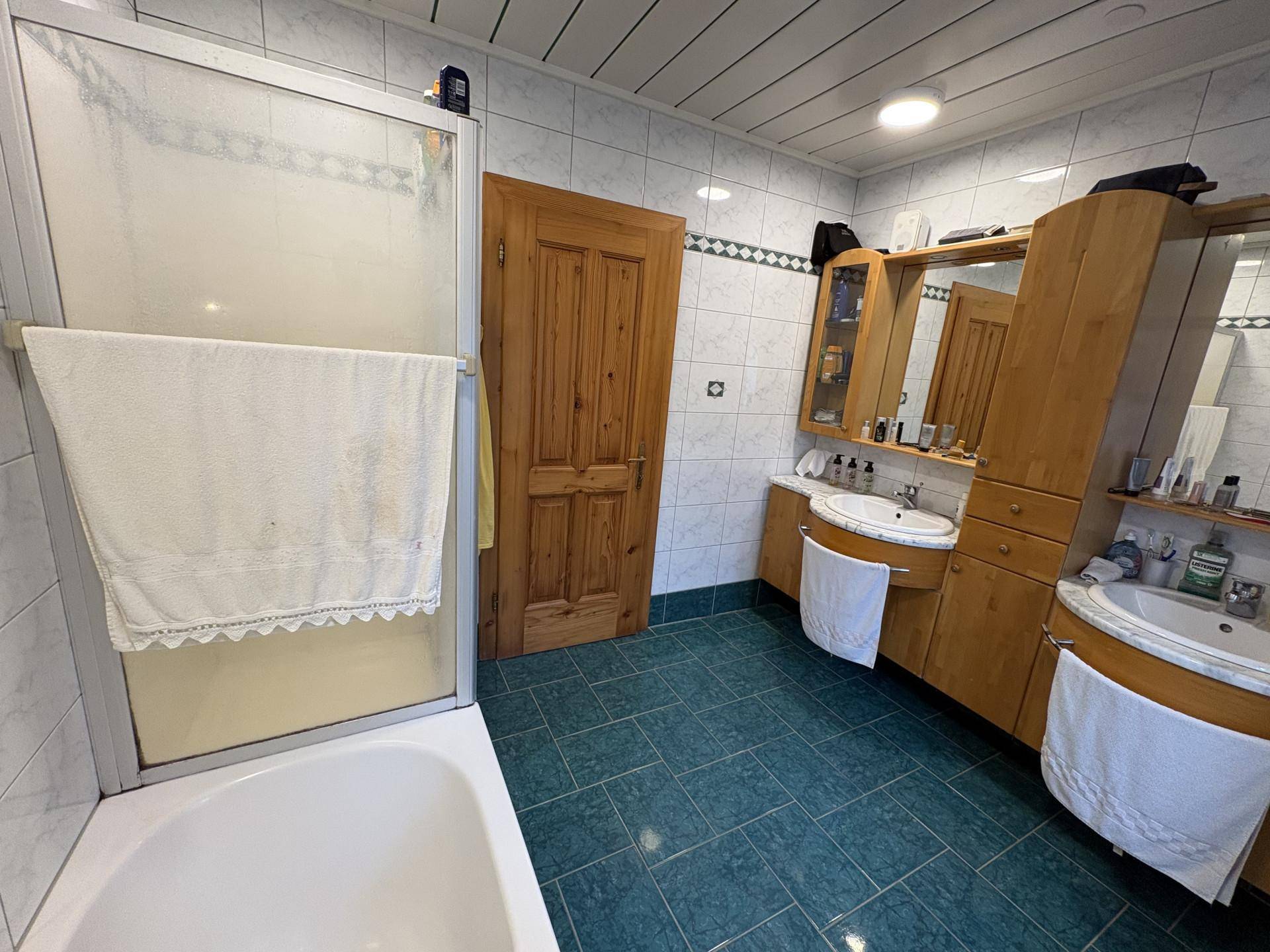 Badezimmer mit Badewanne, Dusche und zwei Waschbecken, ausgestattet mit hellen Fliesen.