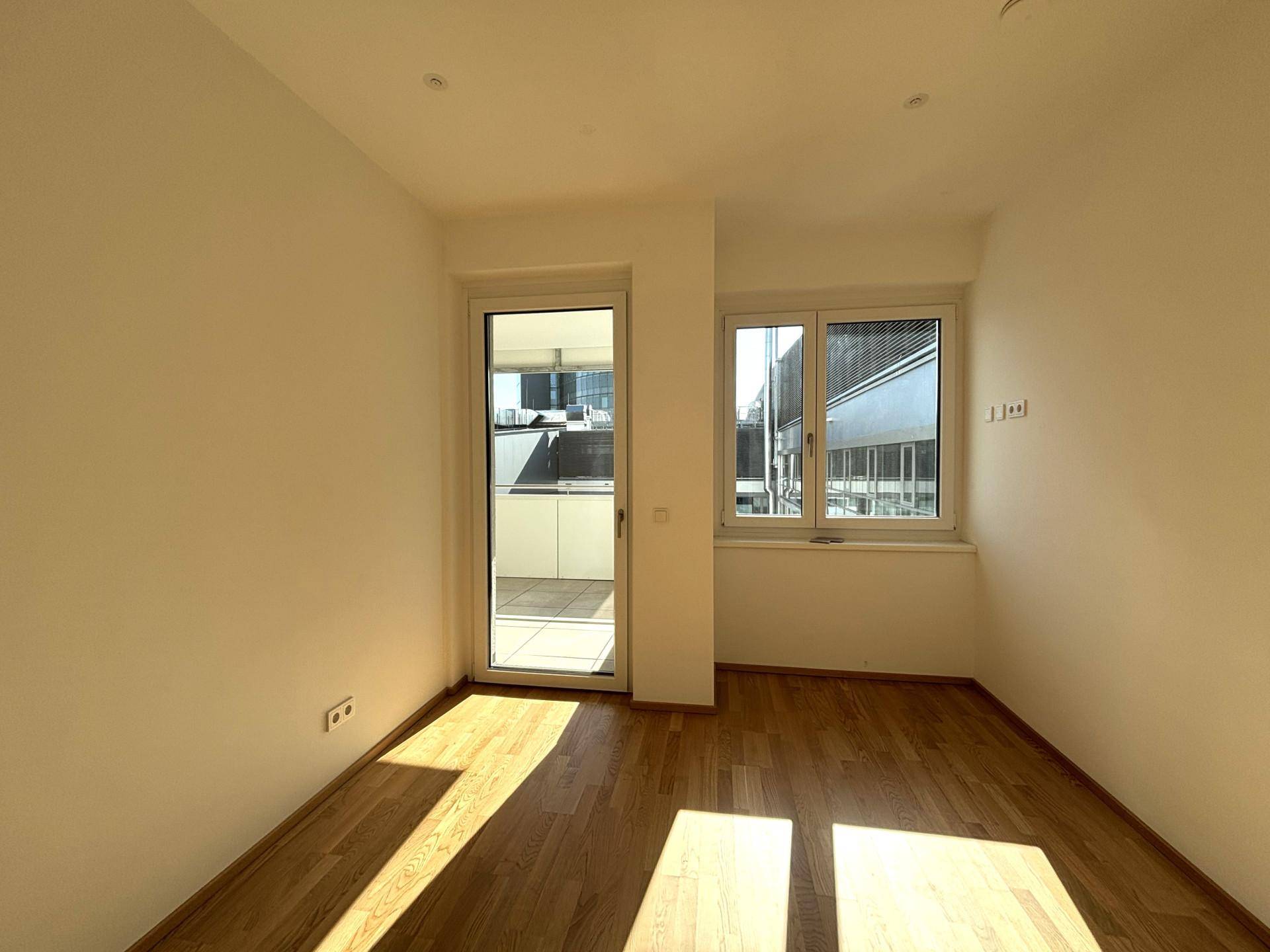 Sonnenverwöhntes Zimmer mit Balkonzugang, Fenster und Parkettboden.