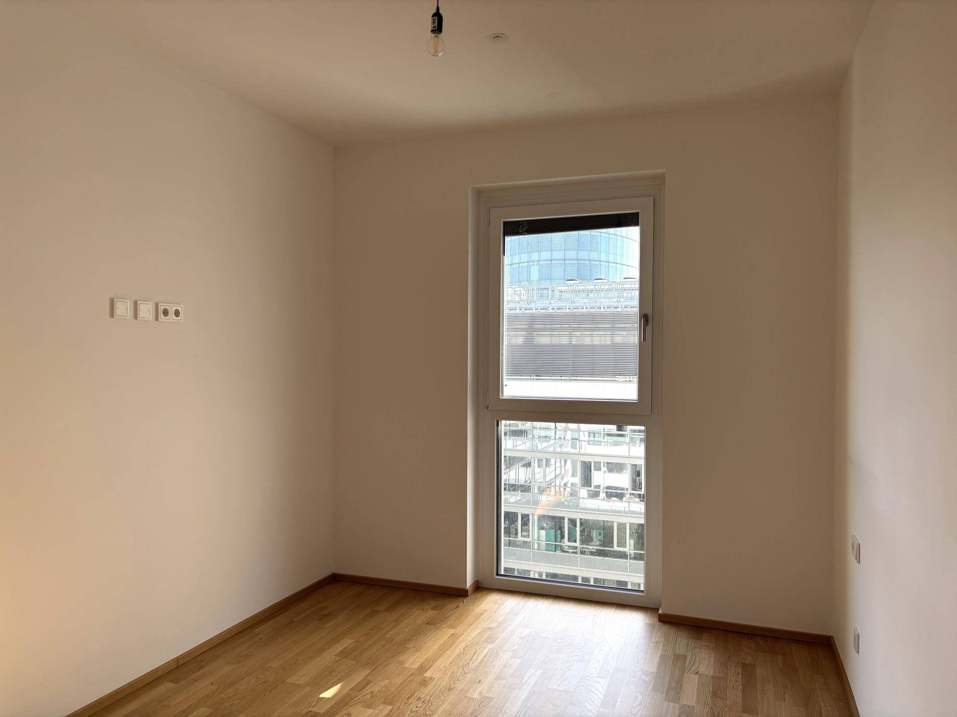 Helles Schlafzimmer mit großem Fenster und Blick auf die Stadtbebauung.