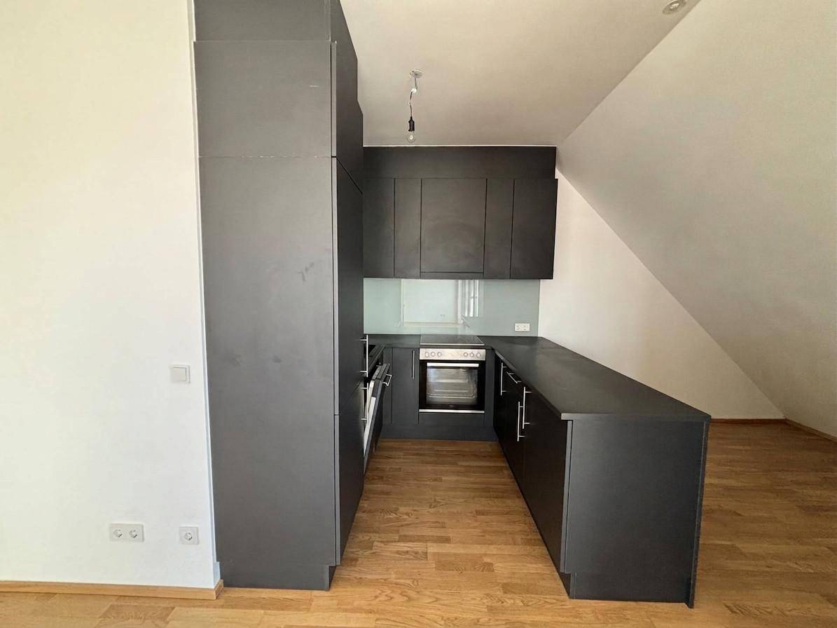 Moderne, dunkle Küche mit Einbaugeräten und Dachschräge in einem hellen Raum.