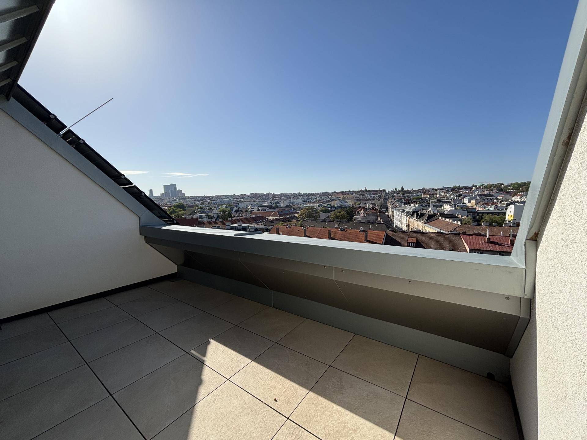 Sonniger Terrassenbereich mit Fliesenboden und weitem Blick über die Stadtlandschaft.