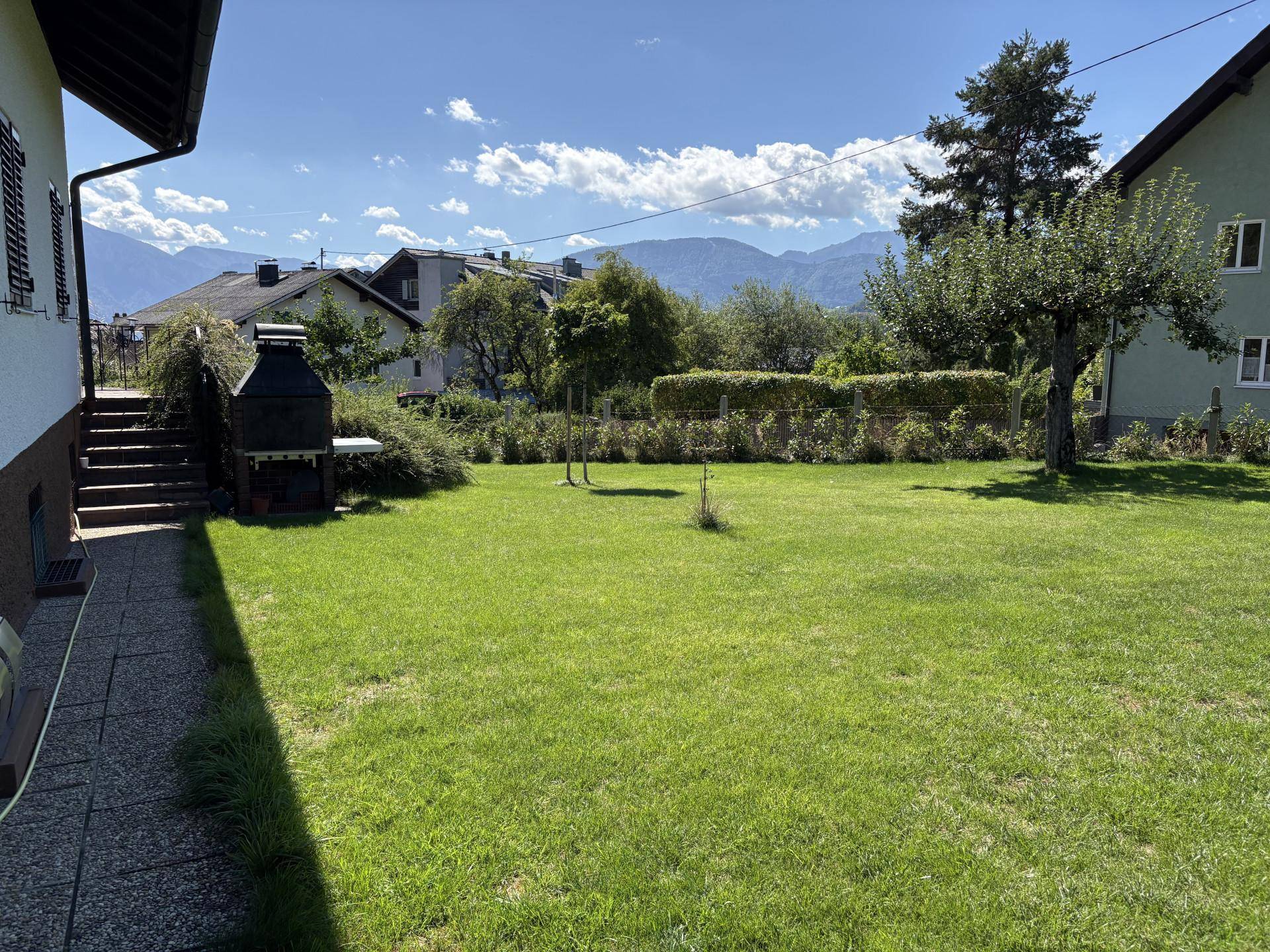 Gepflegter Rasengarten mit Grillplatz neben dem Haus unter blauem Himmel.