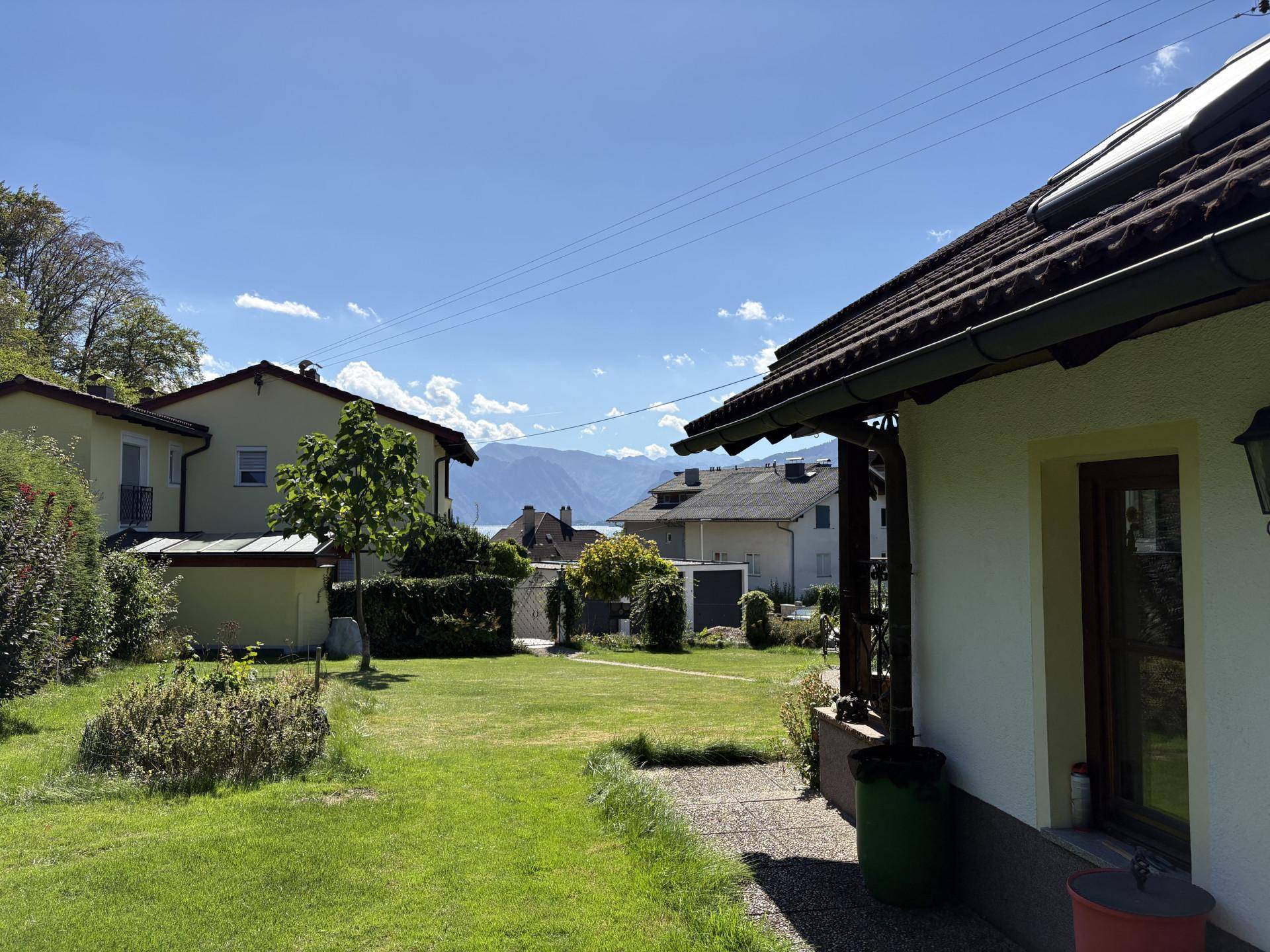 Sonniger Gartenbereich mit Rasen und seitlichem Blick auf den See und die Berge.