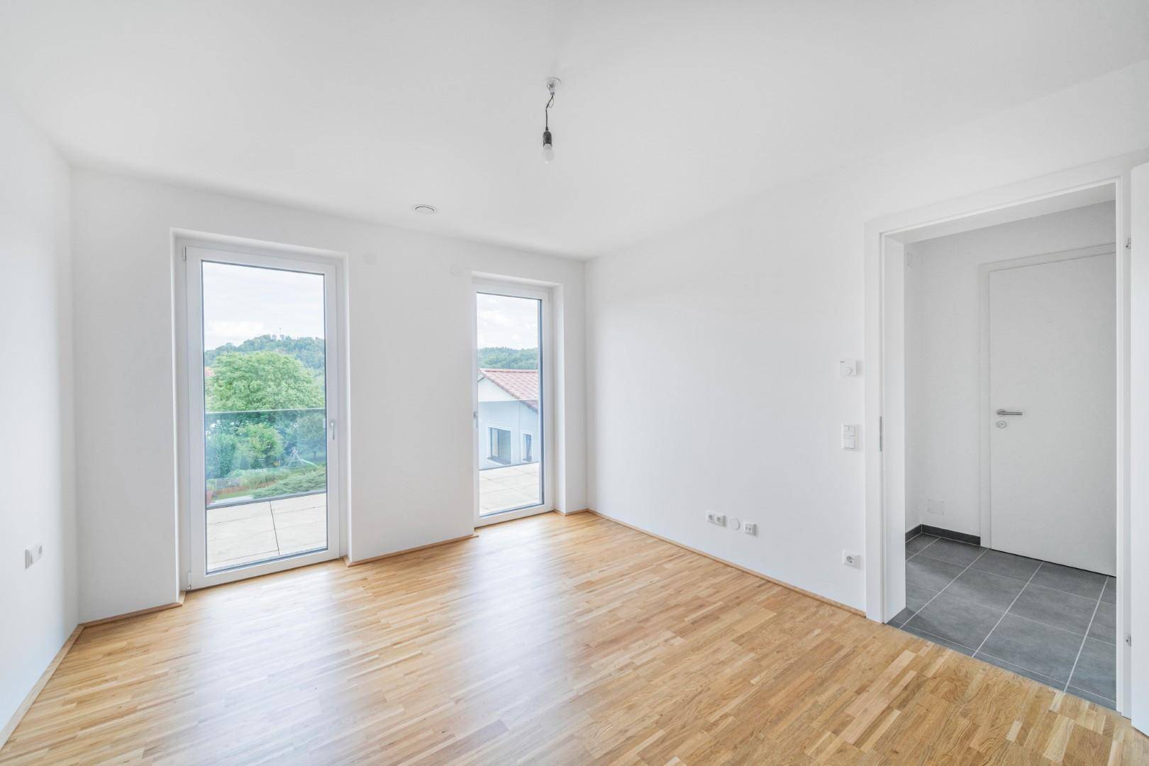 Helles Schlafzimmer mit Holzboden und zwei Fenstertüren, bietet Zugang zu einem kleinen Außenbereich.