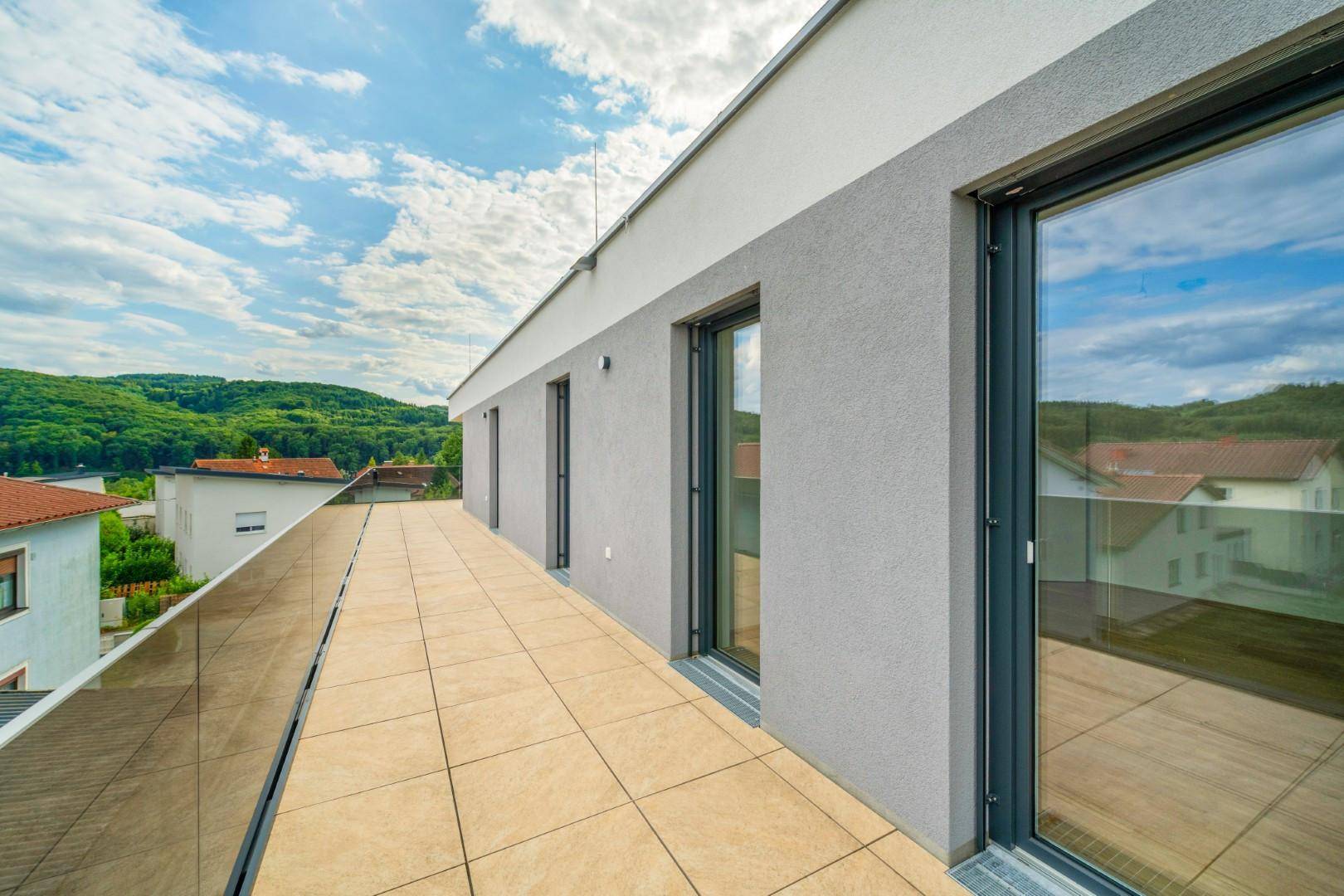 Langer, moderner Balkon mit Fliesenboden und Glasgeländer, bietet einen weiten Blick in die Natur.