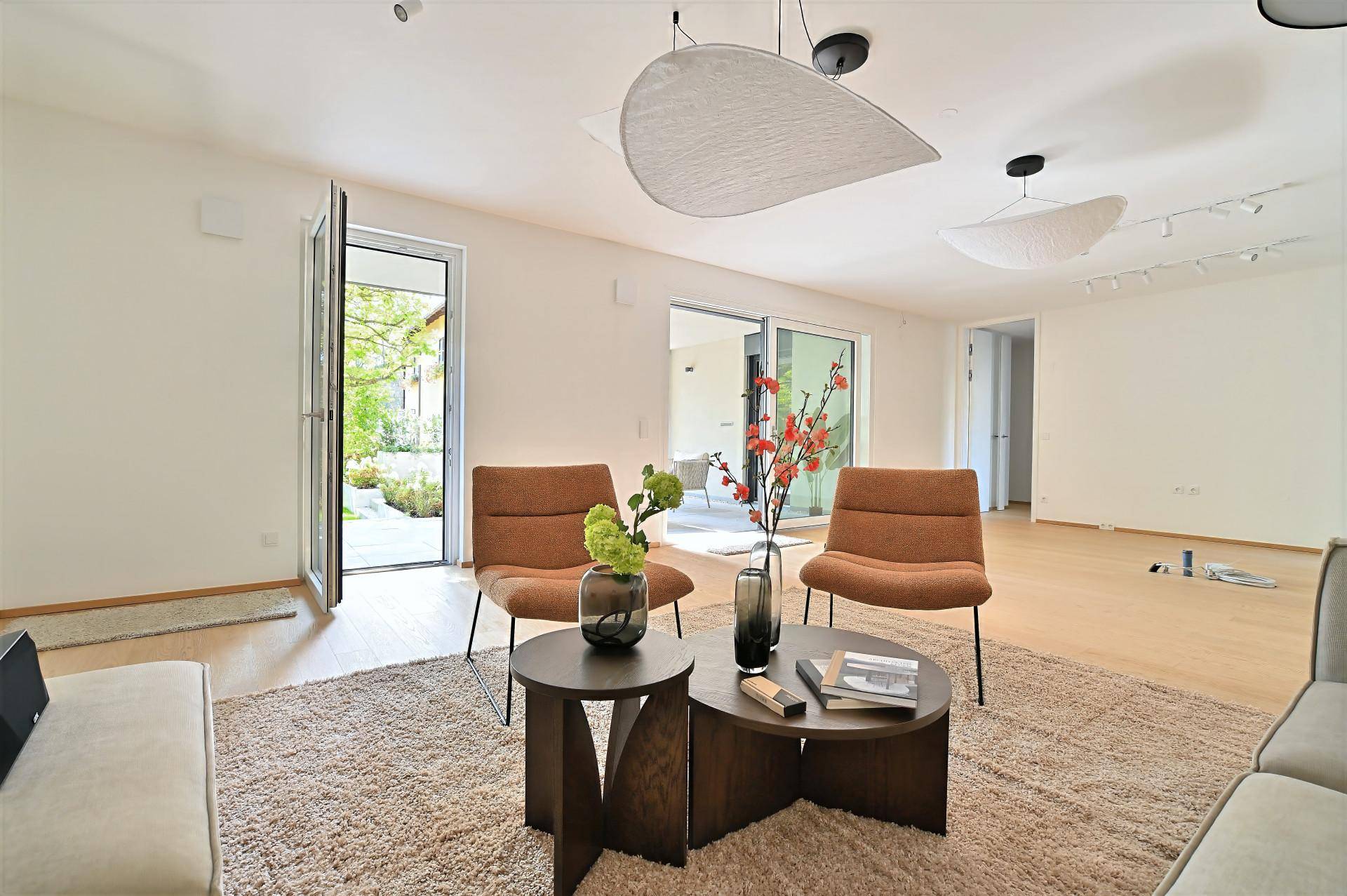 Helles Wohnzimmer mit modernen Möbeln und direktem Zugang zu einem Außenbereich, umgeben von Grün.