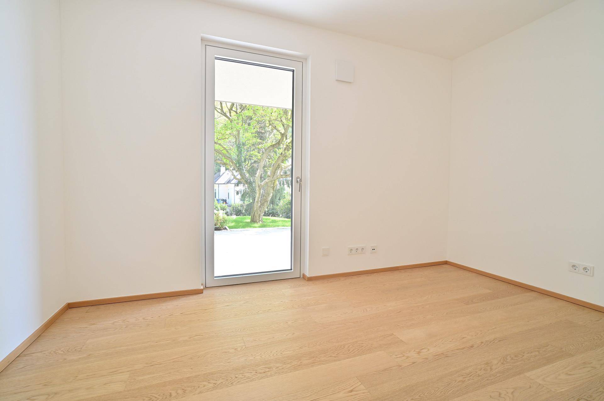 Leeres Zimmer mit Holzboden und einer Glastür, die viel natürliches Licht hereinlässt.