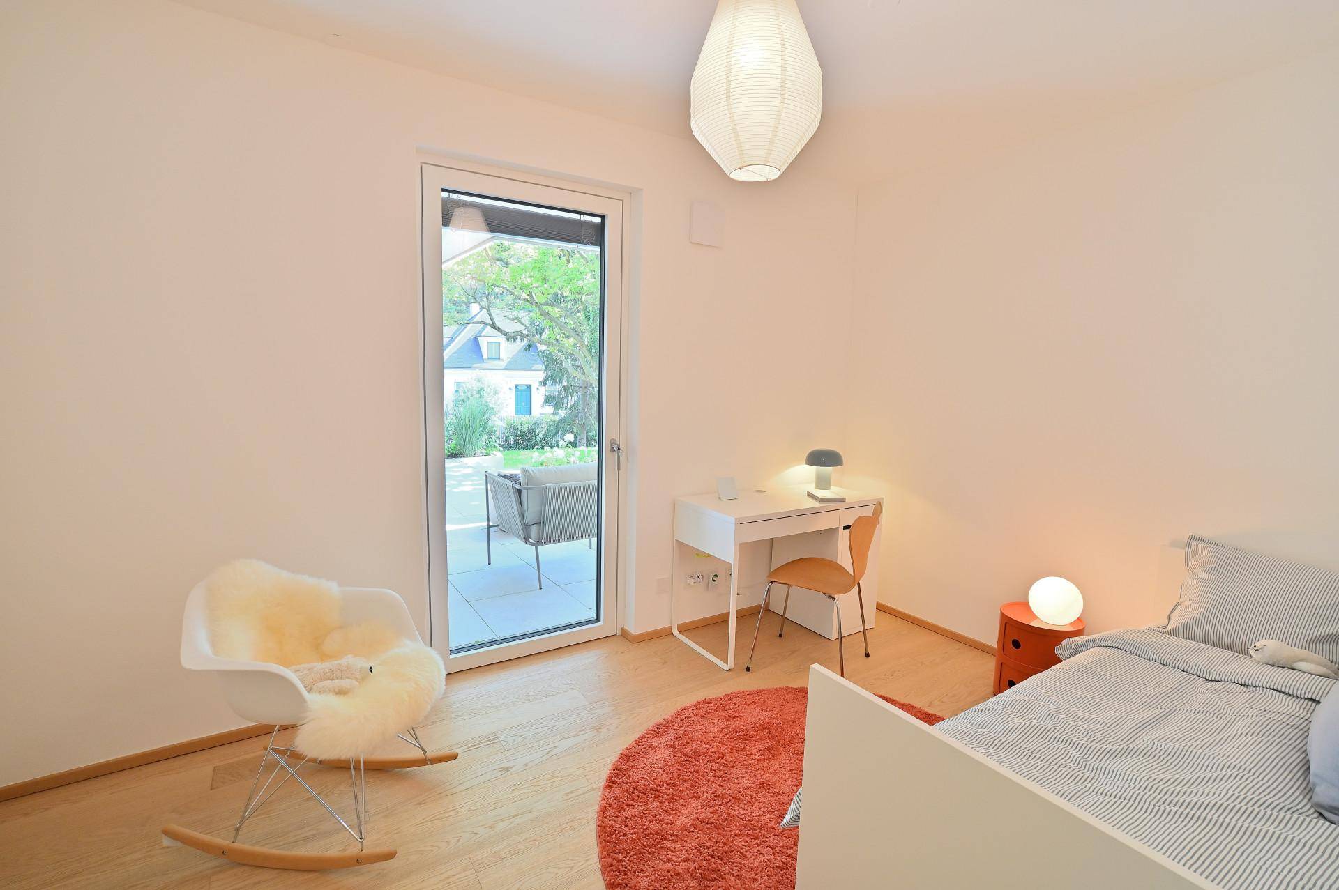 Kinderzimmer oder Gästezimmer mit Holzboden, Schreibtisch und Zugang zu einem Außenbereich.