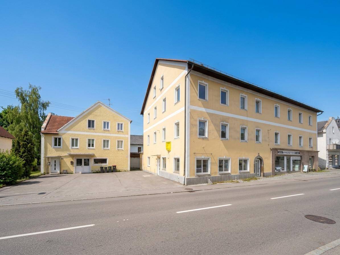 Ansicht von zwei gelben Gebäuden an einer Straße, darunter ein größeres Mehrfamilienhaus und ein kleineres Nebengebäude.