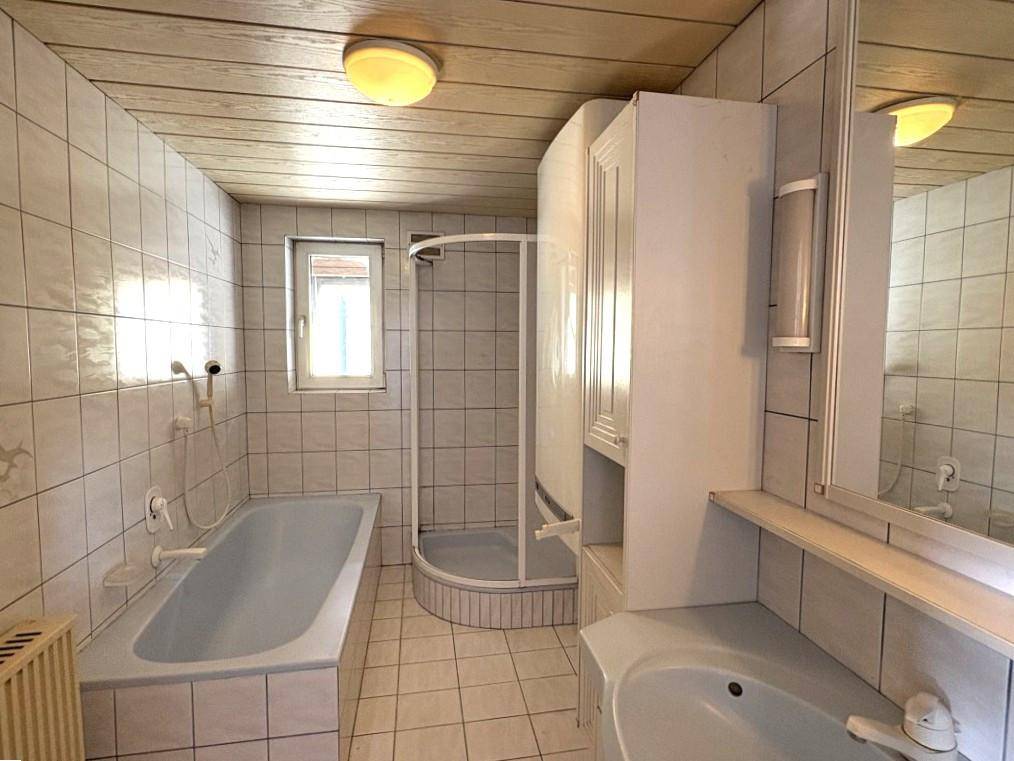 Helles Badezimmer mit Badewanne, Duschkabine, Waschbecken und vollständig gefliesten Wänden und Böden.