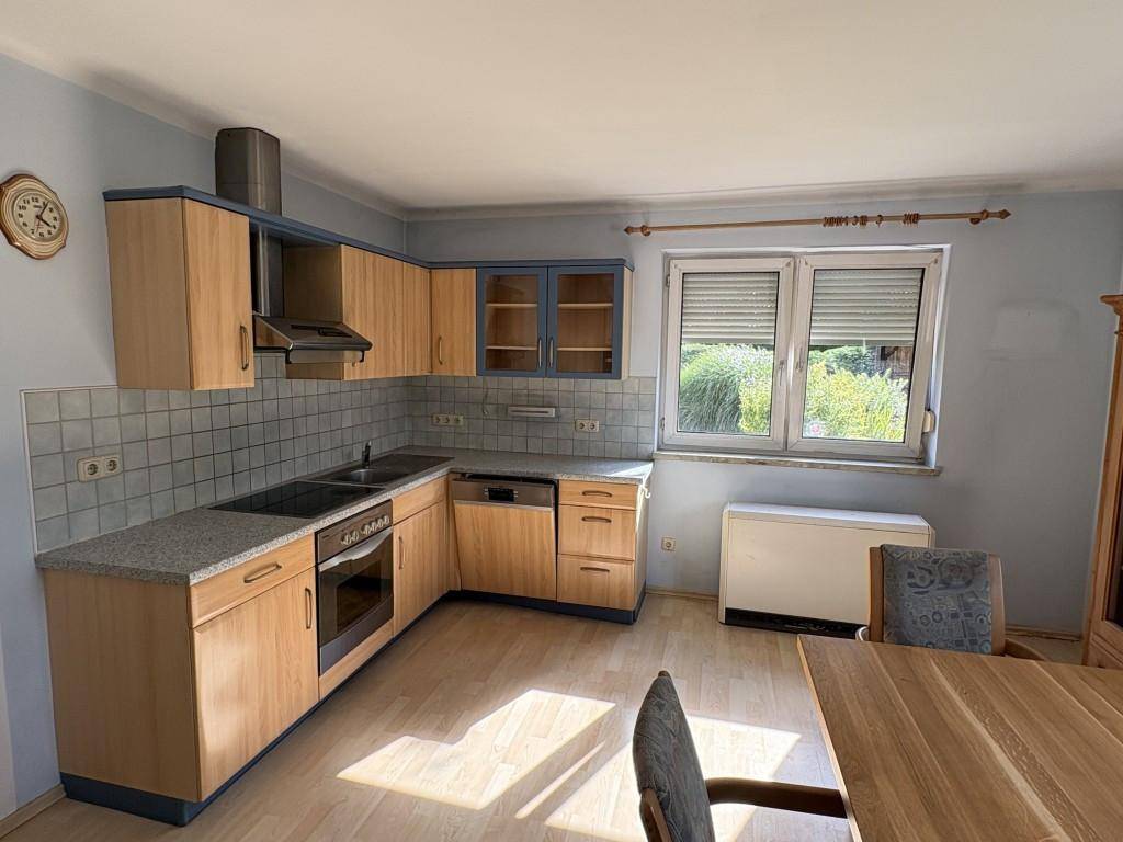 Funktionale Einbauküche mit hellen Holzfronten, Granitarbeitsplatte und Essbereich am Fenster.
