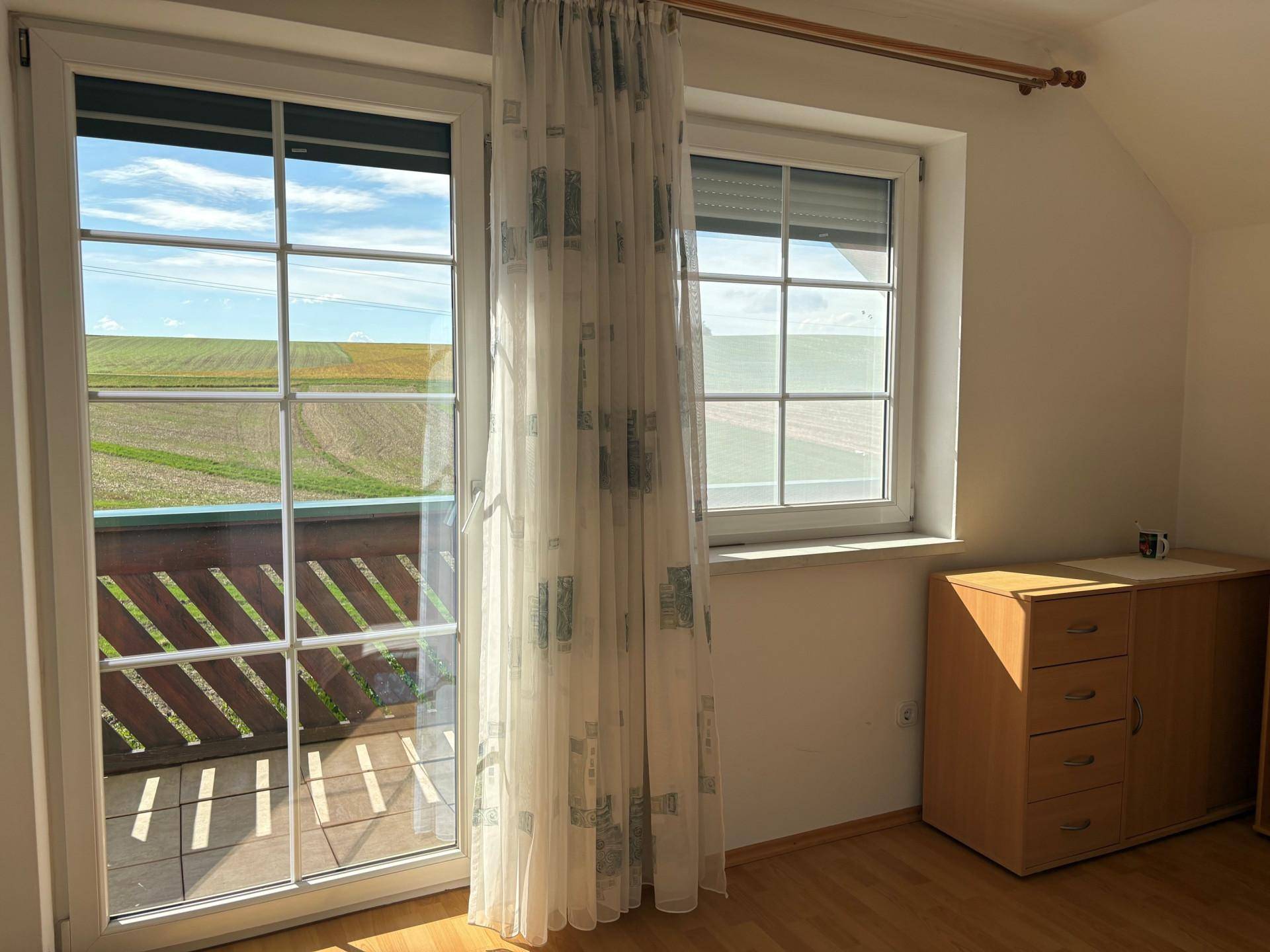 Helles Schlafzimmer mit Balkontür, Fenster und Blick auf die umliegende ländliche Landschaft.