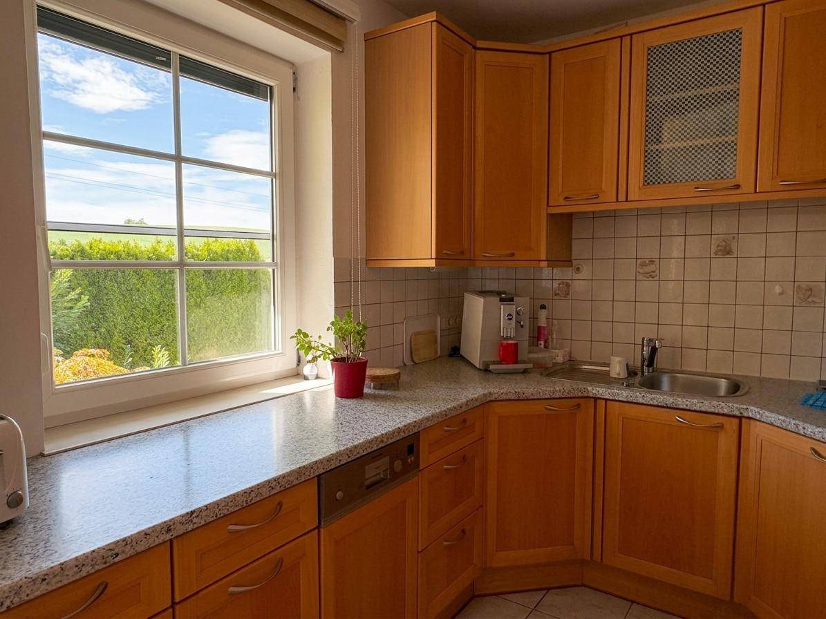 Funktionale Holzküche mit Granitarbeitsplatte, Fliesenrückwand und Fenster mit Blick ins Grüne.