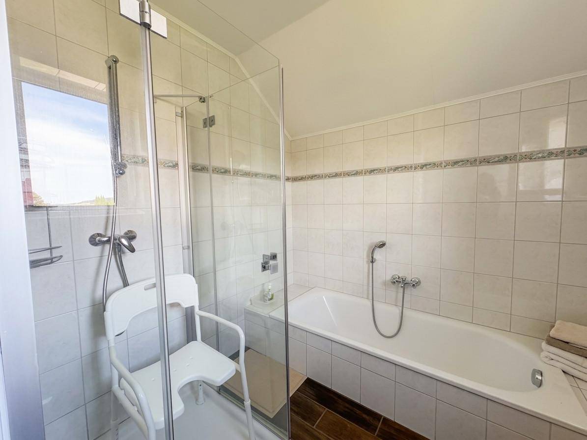 Badezimmer mit Badewanne, Duschkabine, Fliesen und Fenster für natürliches Licht.