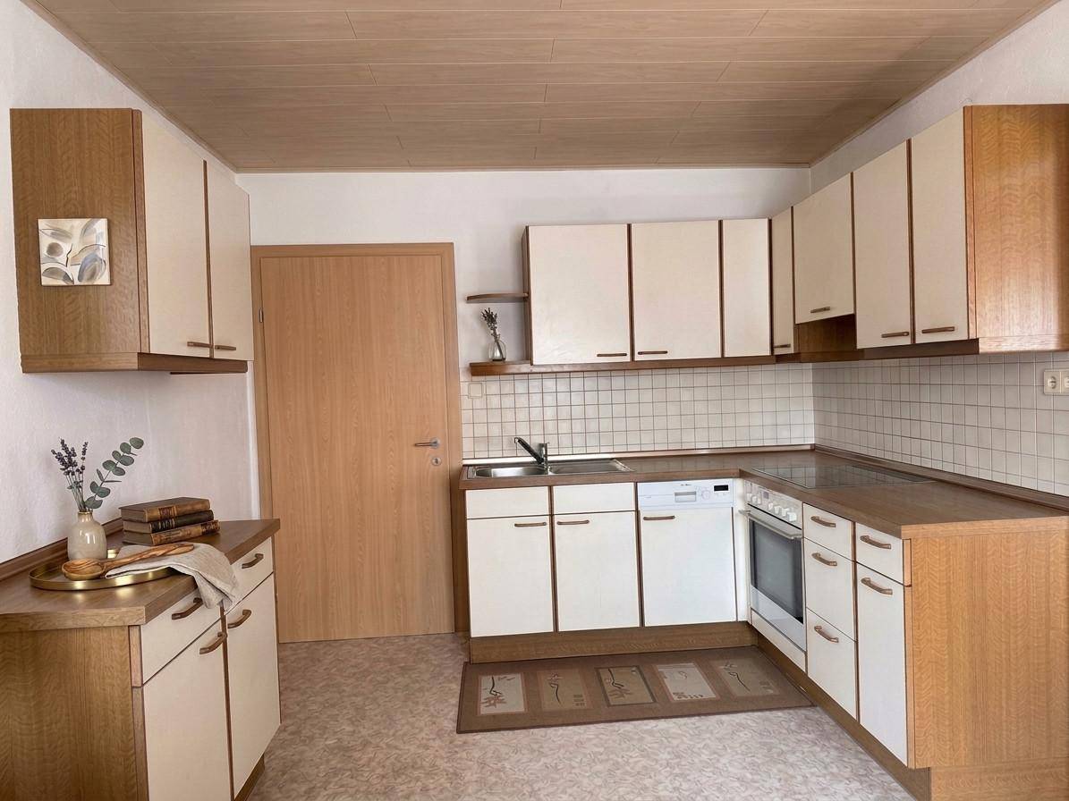 Funktionale Küche mit hellen und holzfarbenen Schränken, ausgestattet mit Spülmaschine und Backofen.