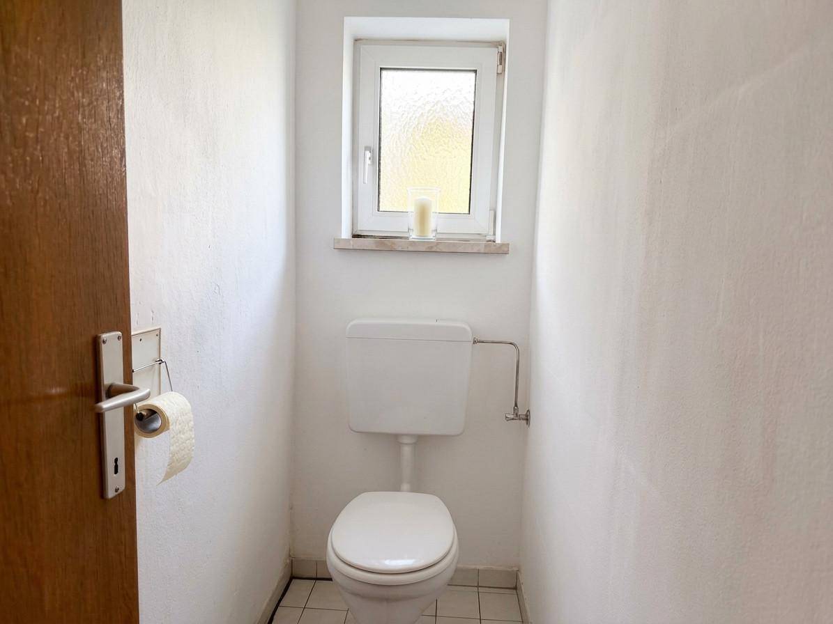 Kleines Gäste-WC mit Toilette und einem Fenster, einfach und funktional gestaltet.