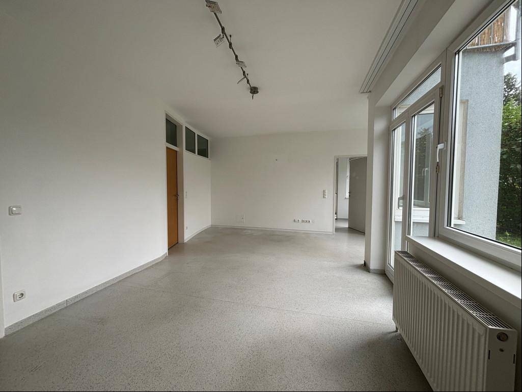 Geräumiger, leerer Raum mit großen Fenstern und Zugang zum Außenbereich.