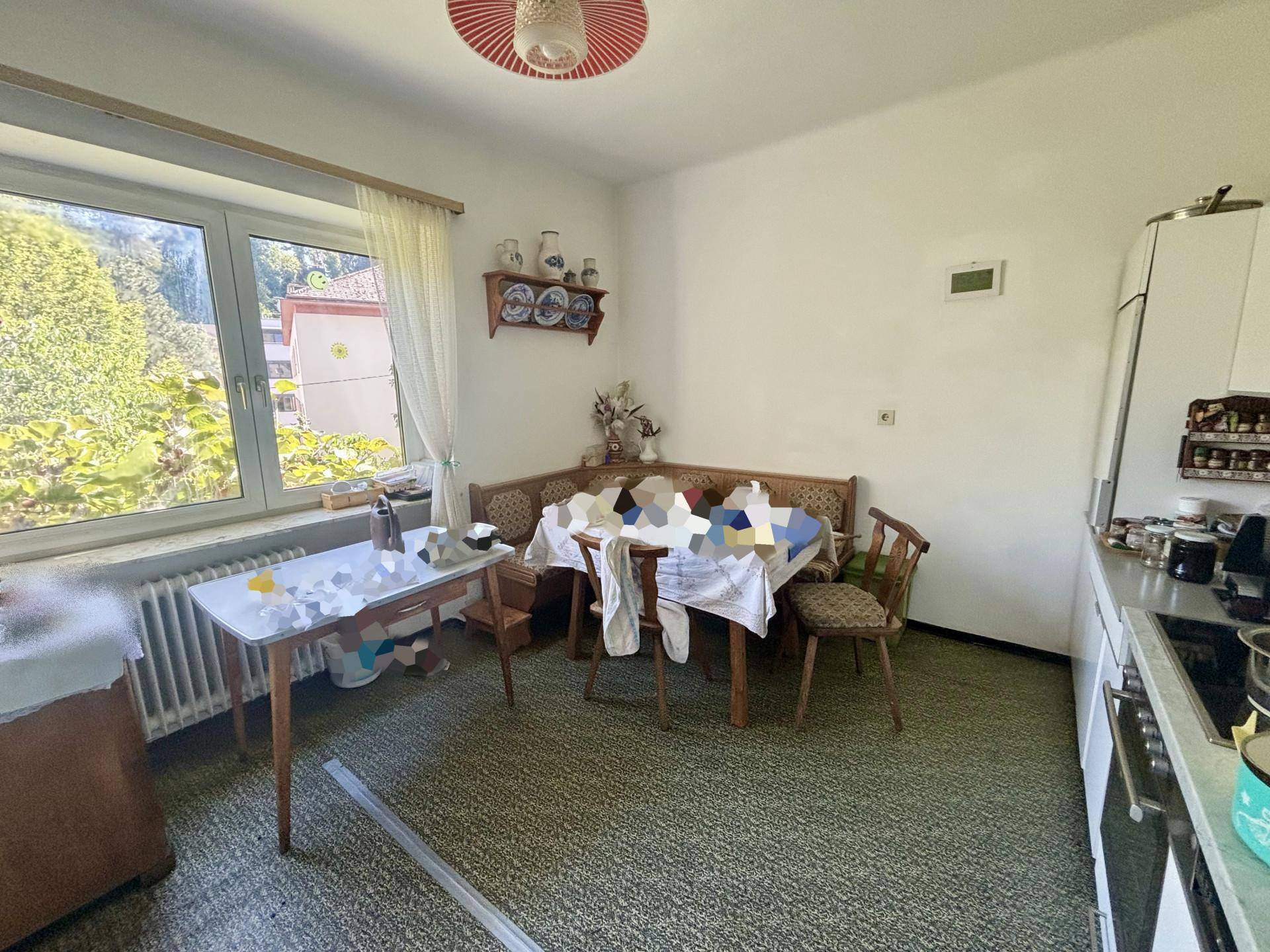 Gemütliche Wohnküche mit Esstisch, Fenster und Blick ins Grüne, ausgestattet mit älteren Möbeln.