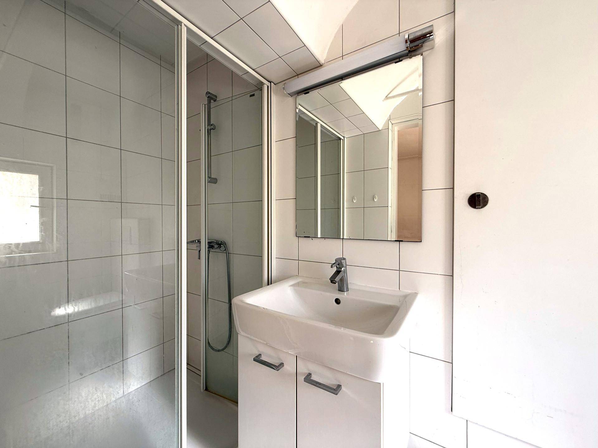 Modernisiertes Badezimmer mit Duschkabine, Waschbecken und Spiegel, hell gefliest.