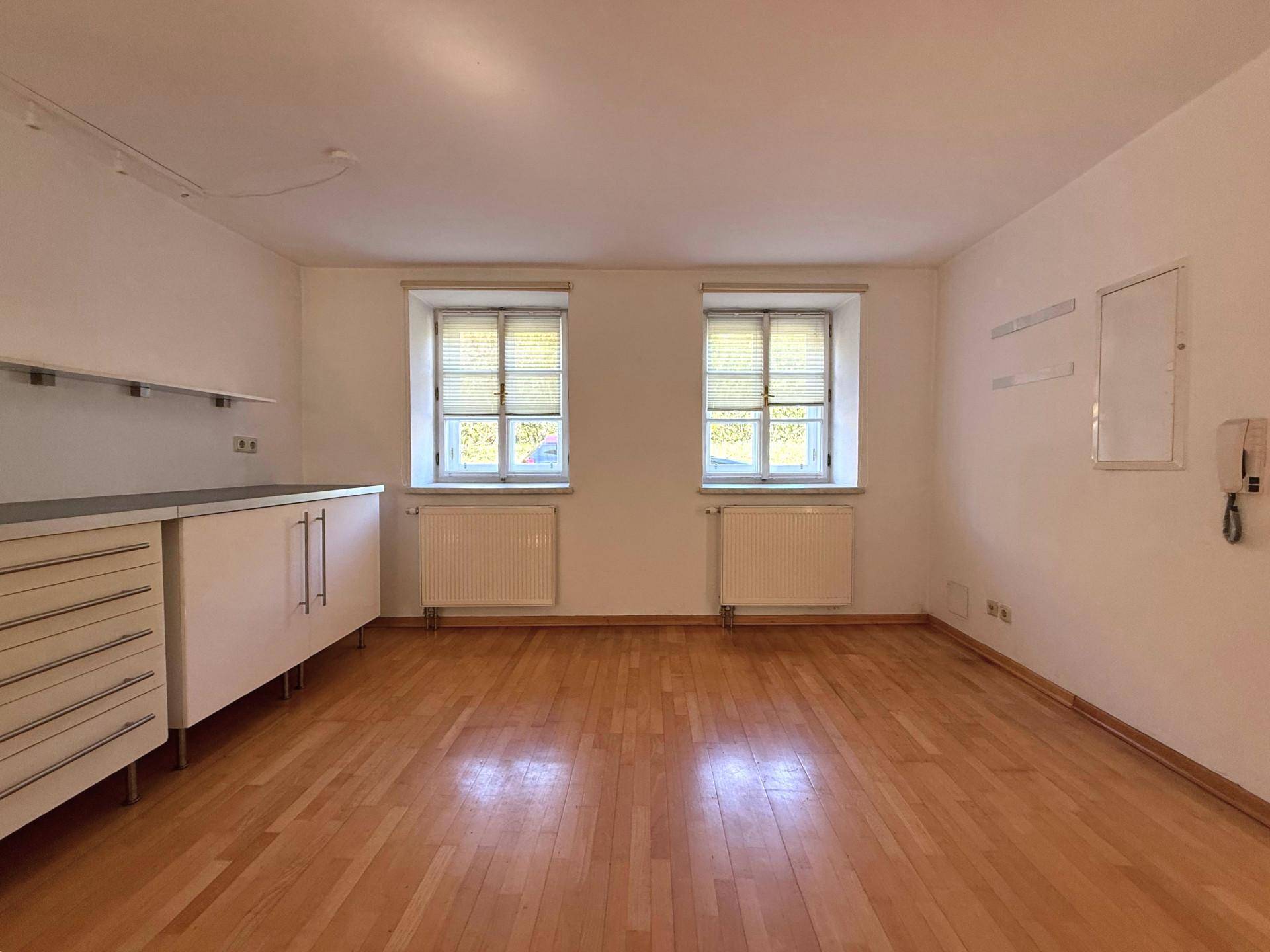 Leerer Raum mit Holzboden, zwei Fenstern und Heizkörpern, bereit zur individuellen Gestaltung.
