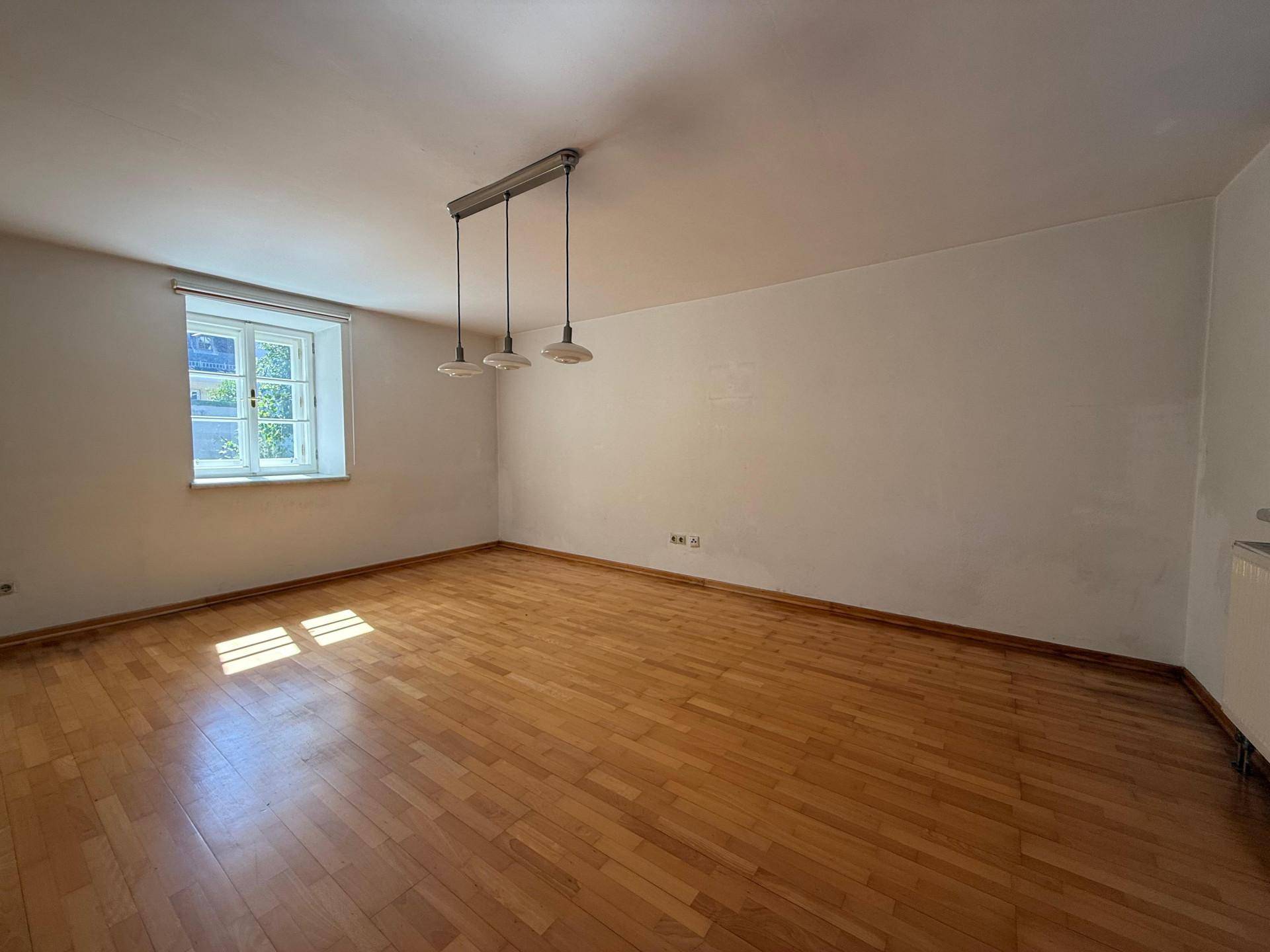 Helles Wohnzimmer mit Holzboden, einem Fenster und einer modernen Deckenleuchte.