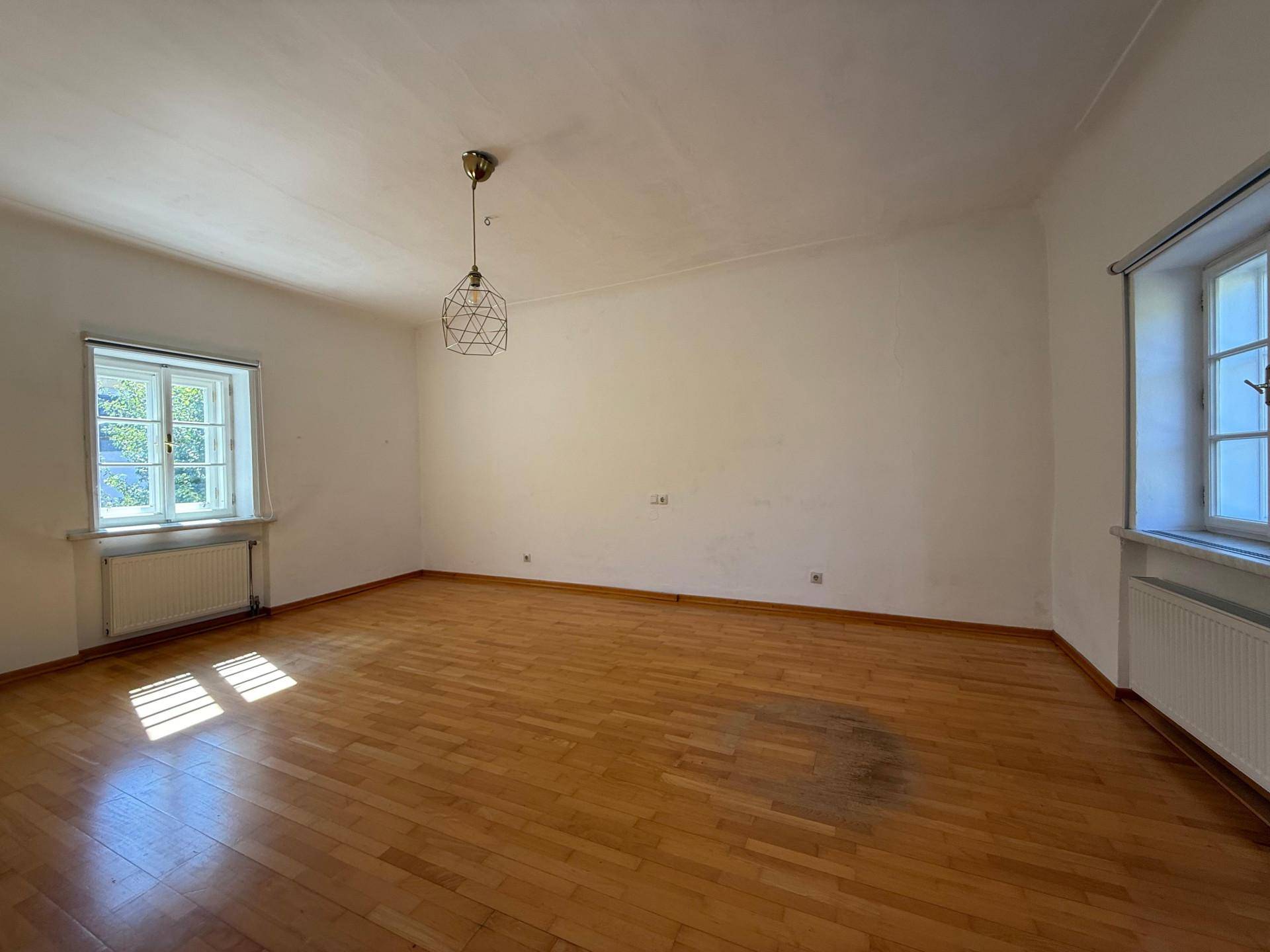 Helles Wohnzimmer mit Holzboden, einem Fenster und einer modernen Pendelleuchte.