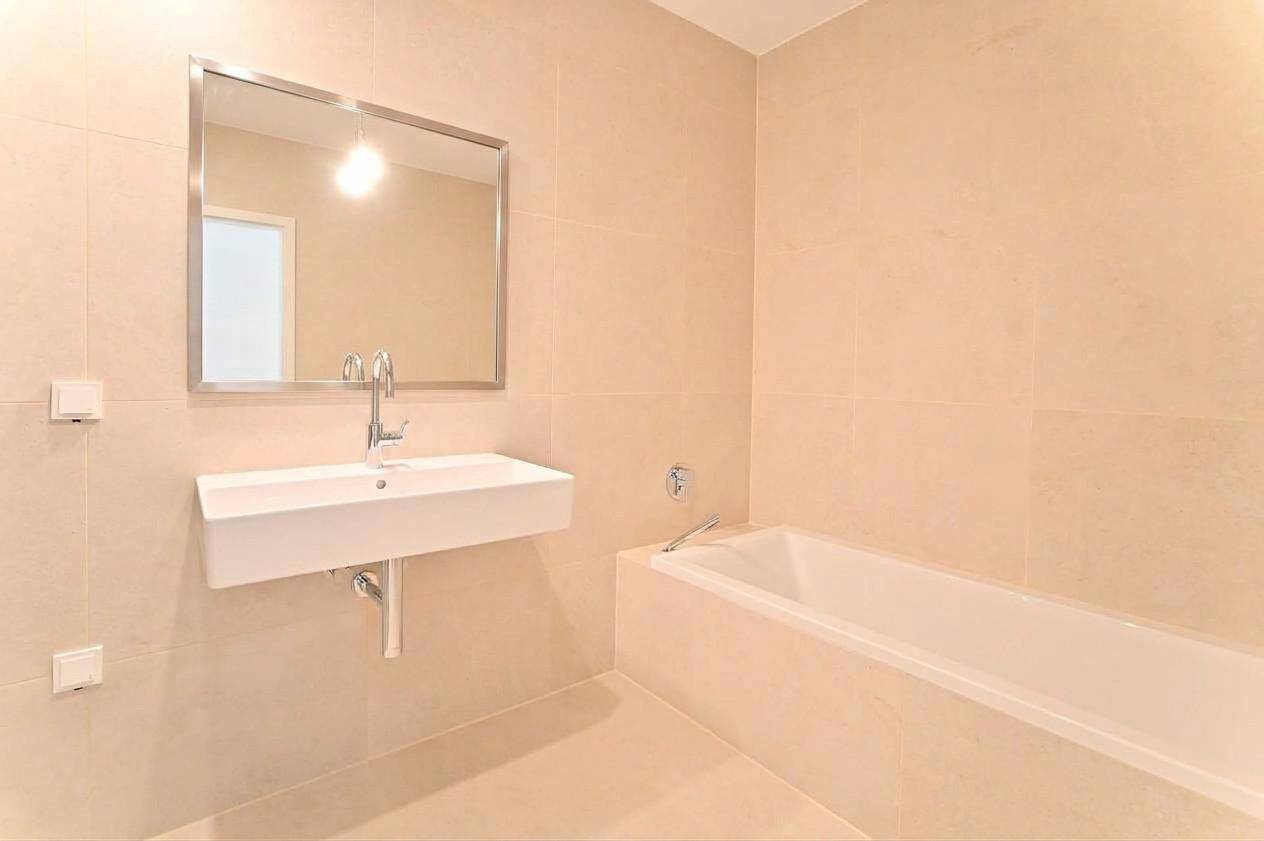 Helles Badezimmer mit Wandwaschbecken, Badewanne und einem modernen Spiegel über dem Waschtisch.