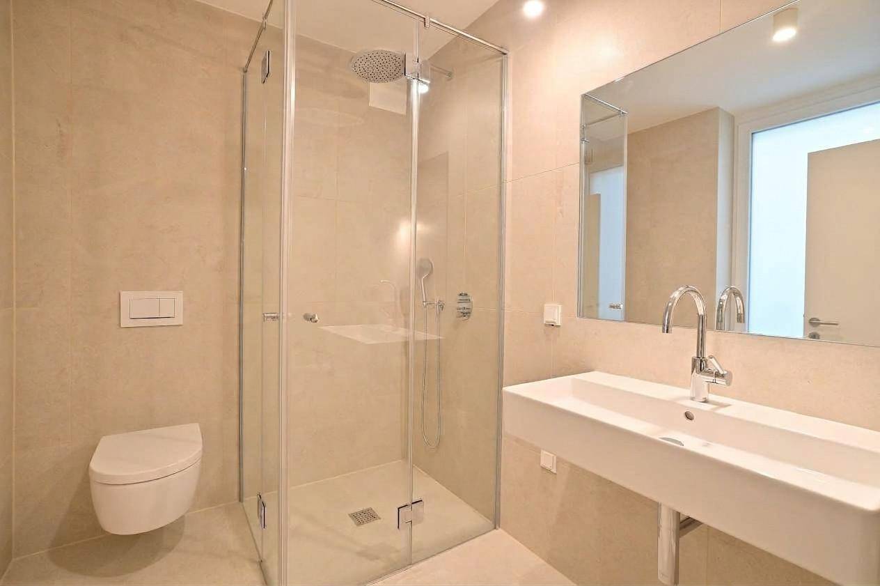Modernes Badezimmer mit beigefarbenen Fliesen, Dusche, WC, Waschbecken und Spiegel.