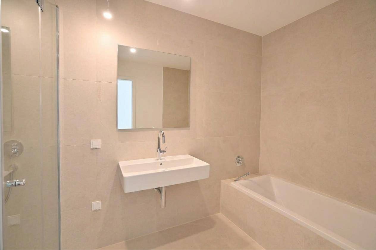 Modernes Badezimmer mit beigefarbenen Fliesen, Waschbecken, Spiegel und Badewanne.