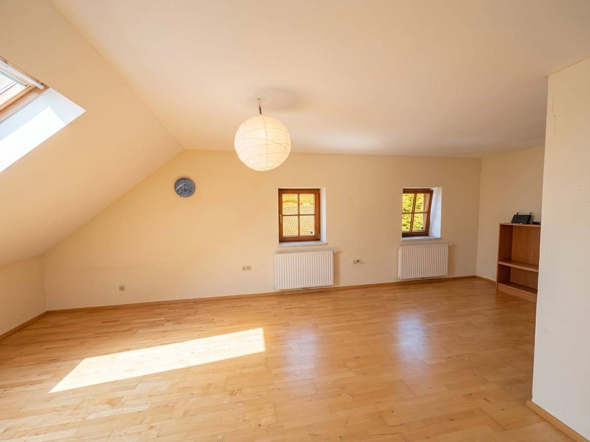 Heller Dachbodenraum mit Holzboden, Dachfenster und zwei kleineren Fenstern, ideal als Schlafzimmer.