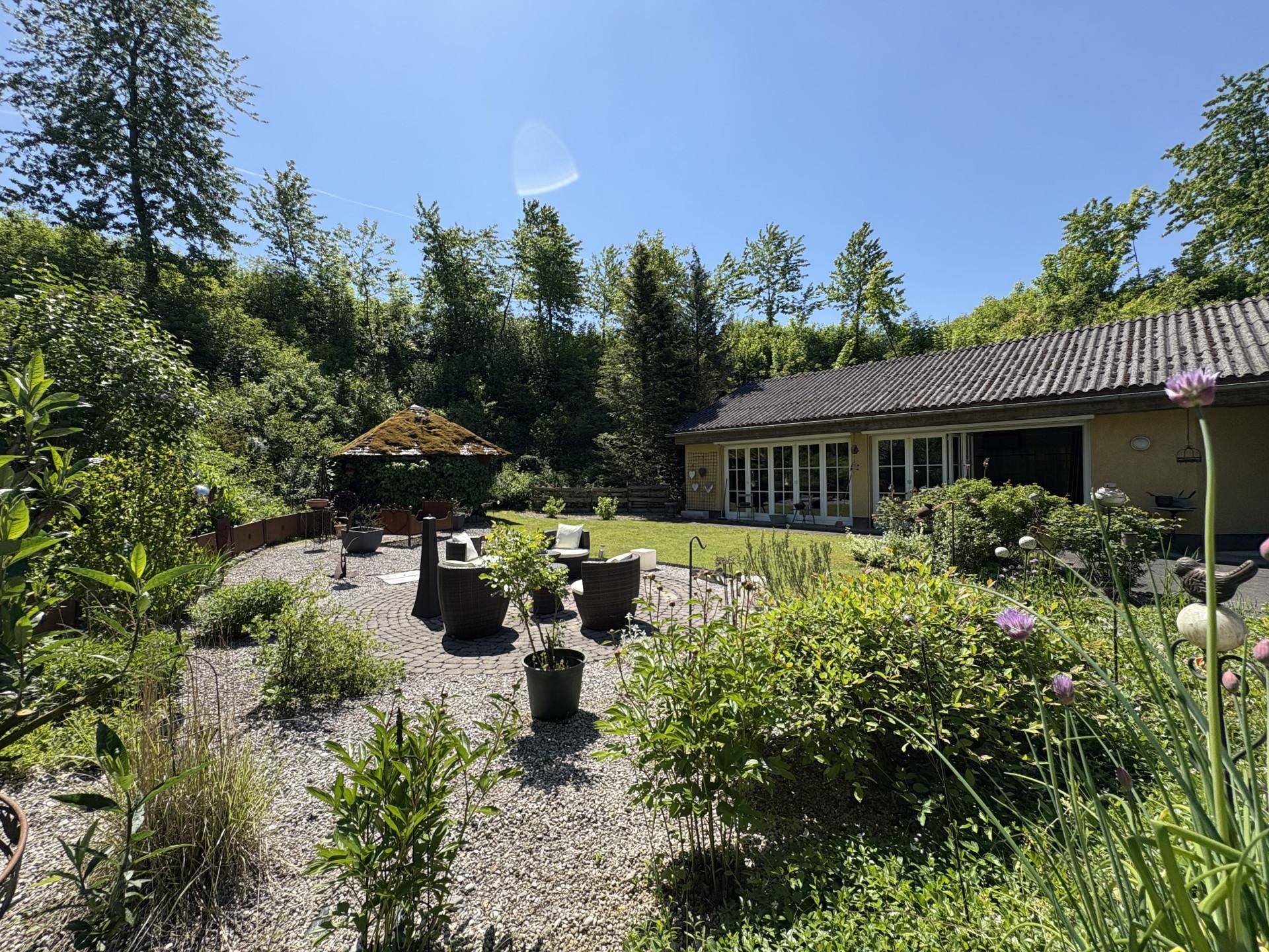 Weitläufiger Garten mit verschiedenen Sitzbereichen, üppiger Bepflanzung und Gartenhaus.