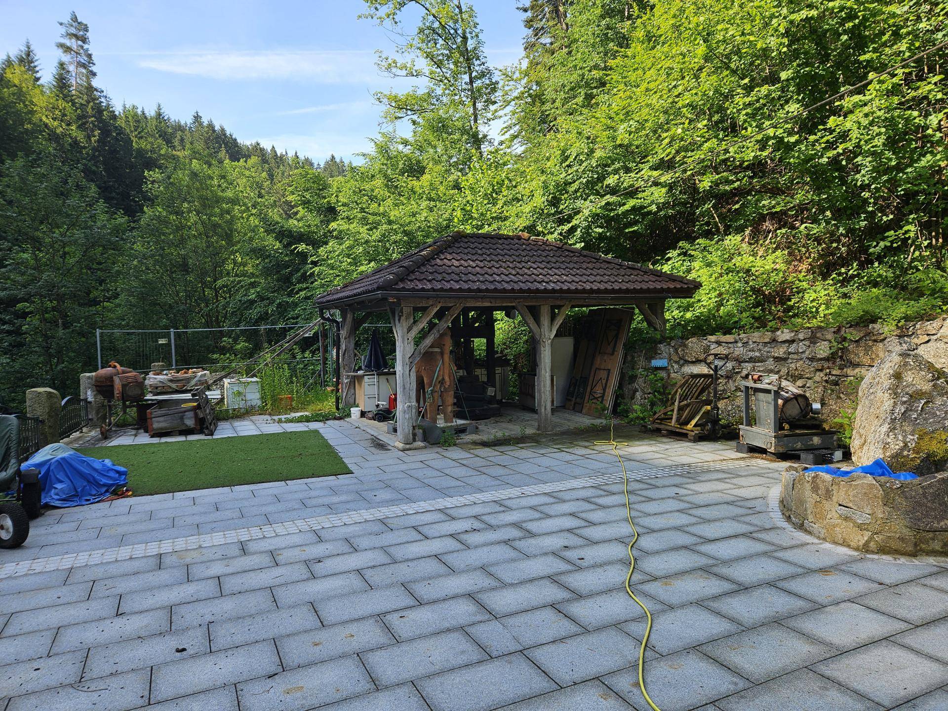 Große gepflasterte Terrasse mit einem Holzpavillon und umgebender Natur, ideal für Entspannung im Freien.