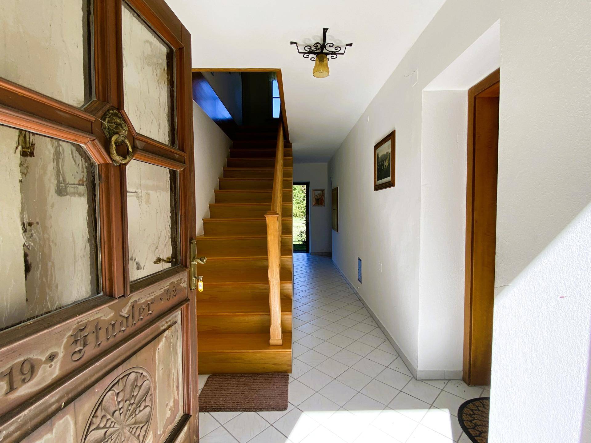 Heller Eingangsbereich mit gefliestem Boden und Holztreppe zum Obergeschoss.