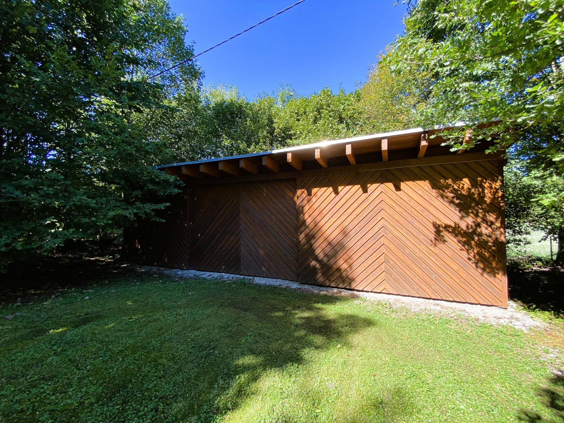 Geräumiger Holzschuppen mit moderner Holzverkleidung und schrägem Dach im Grünen.