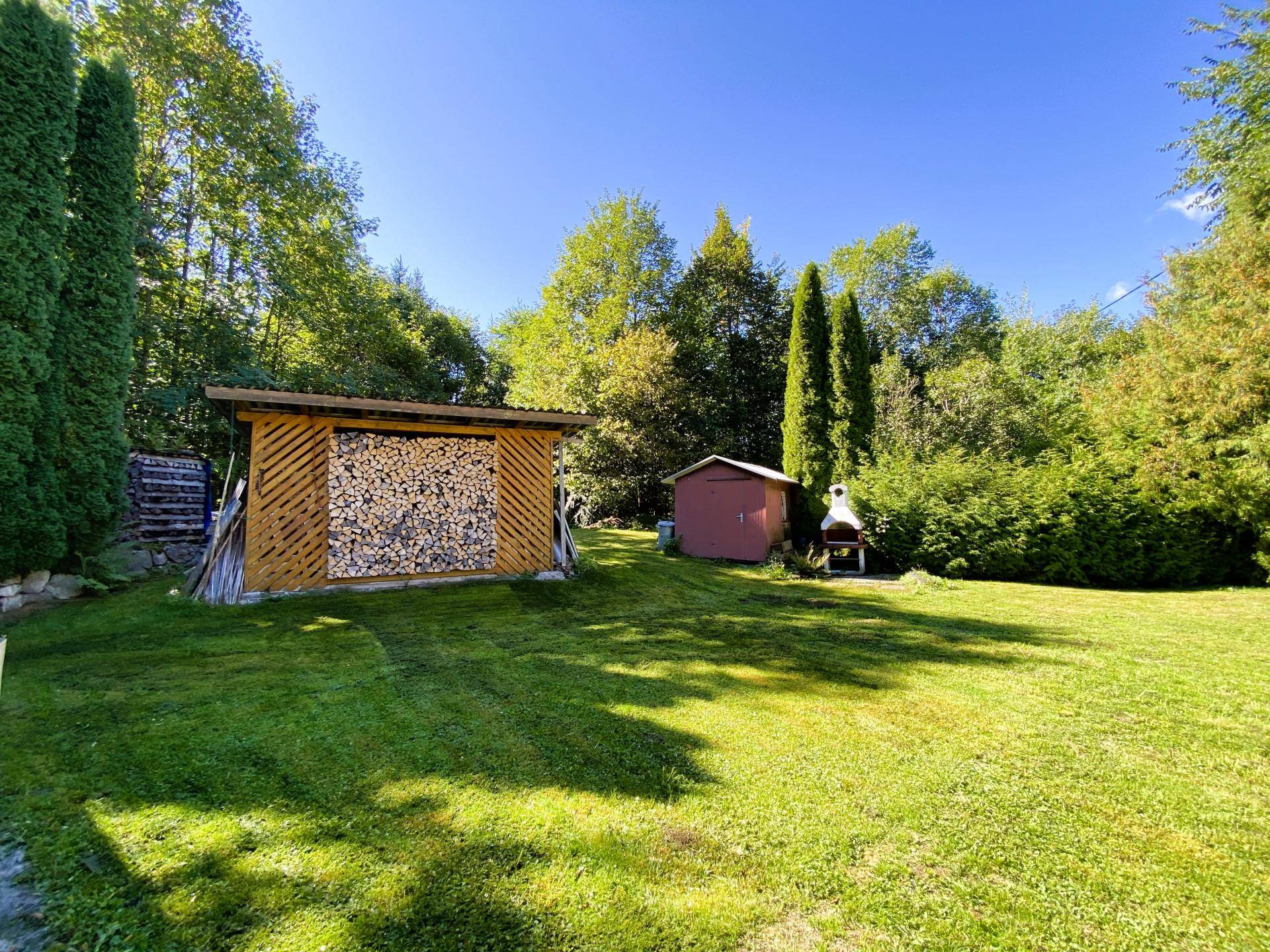 Großer Gartenbereich mit Holzschuppen, Brennholzstapel und Grillplatz.