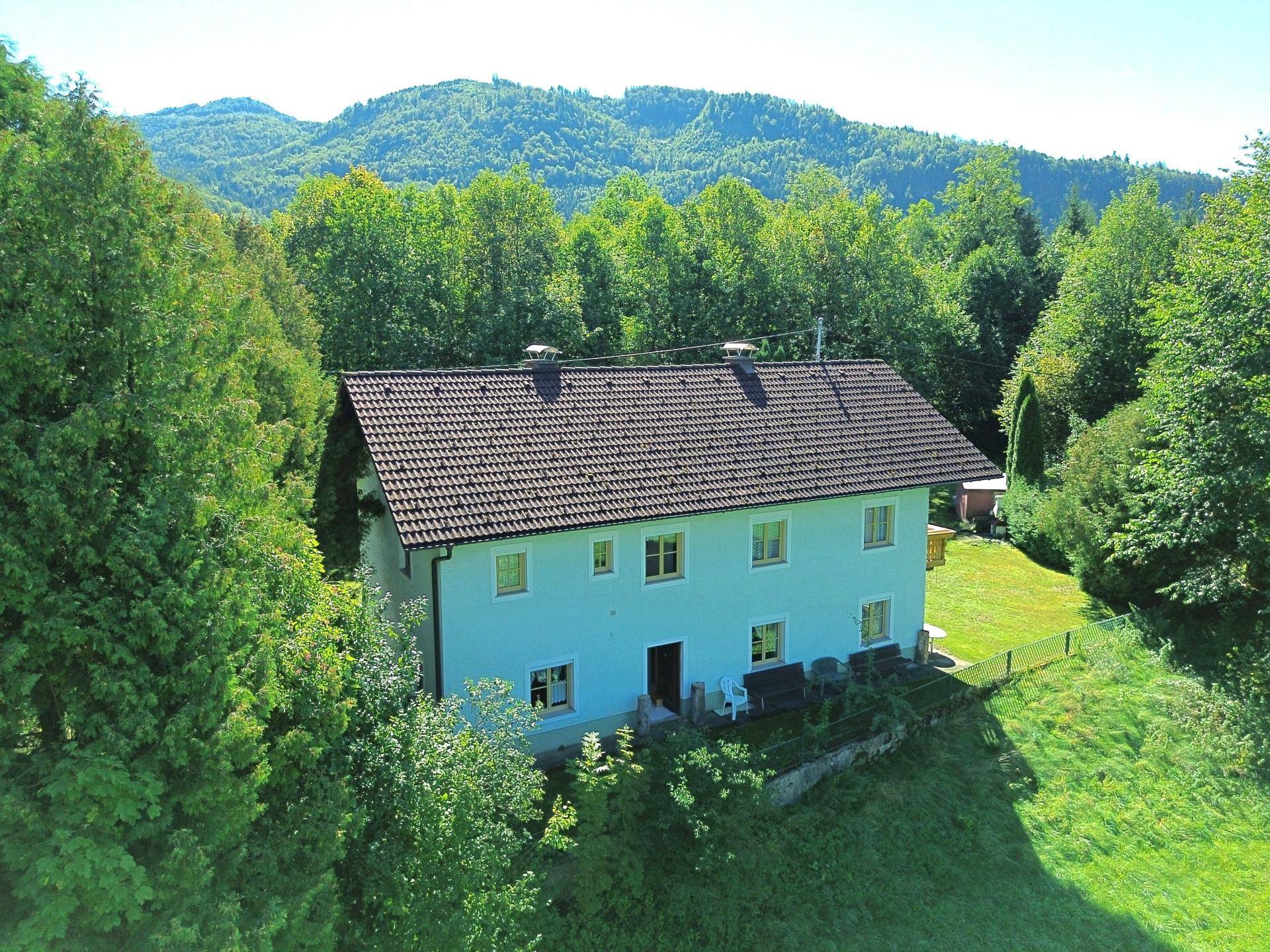 Luftaufnahme eines Hauses umgeben von üppiger grüner Natur und Bergen.